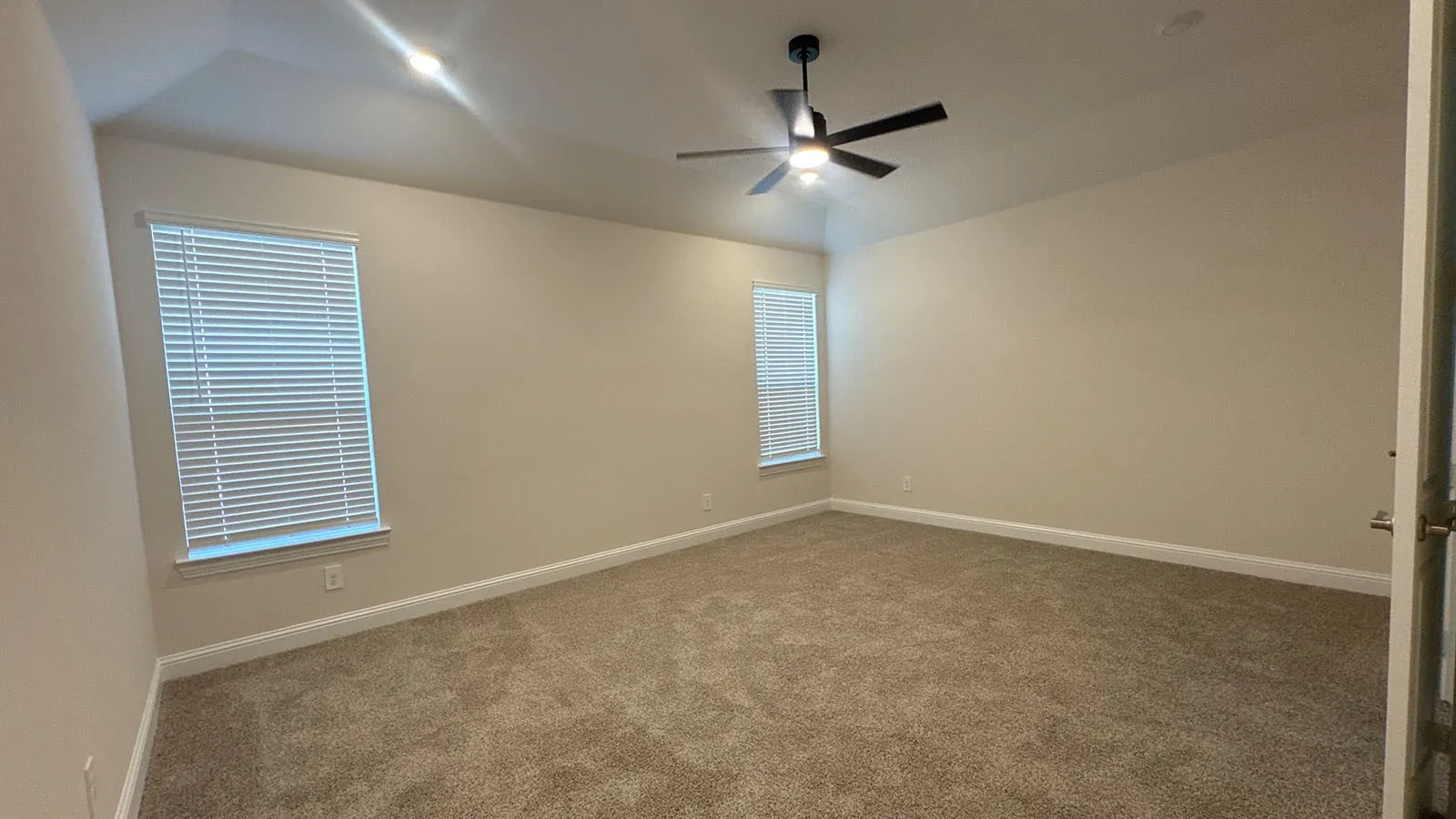 Spacious room featuring neutral carpet, two windows with blinds, a ceiling fan with integrated lighting, and neutral wall paint