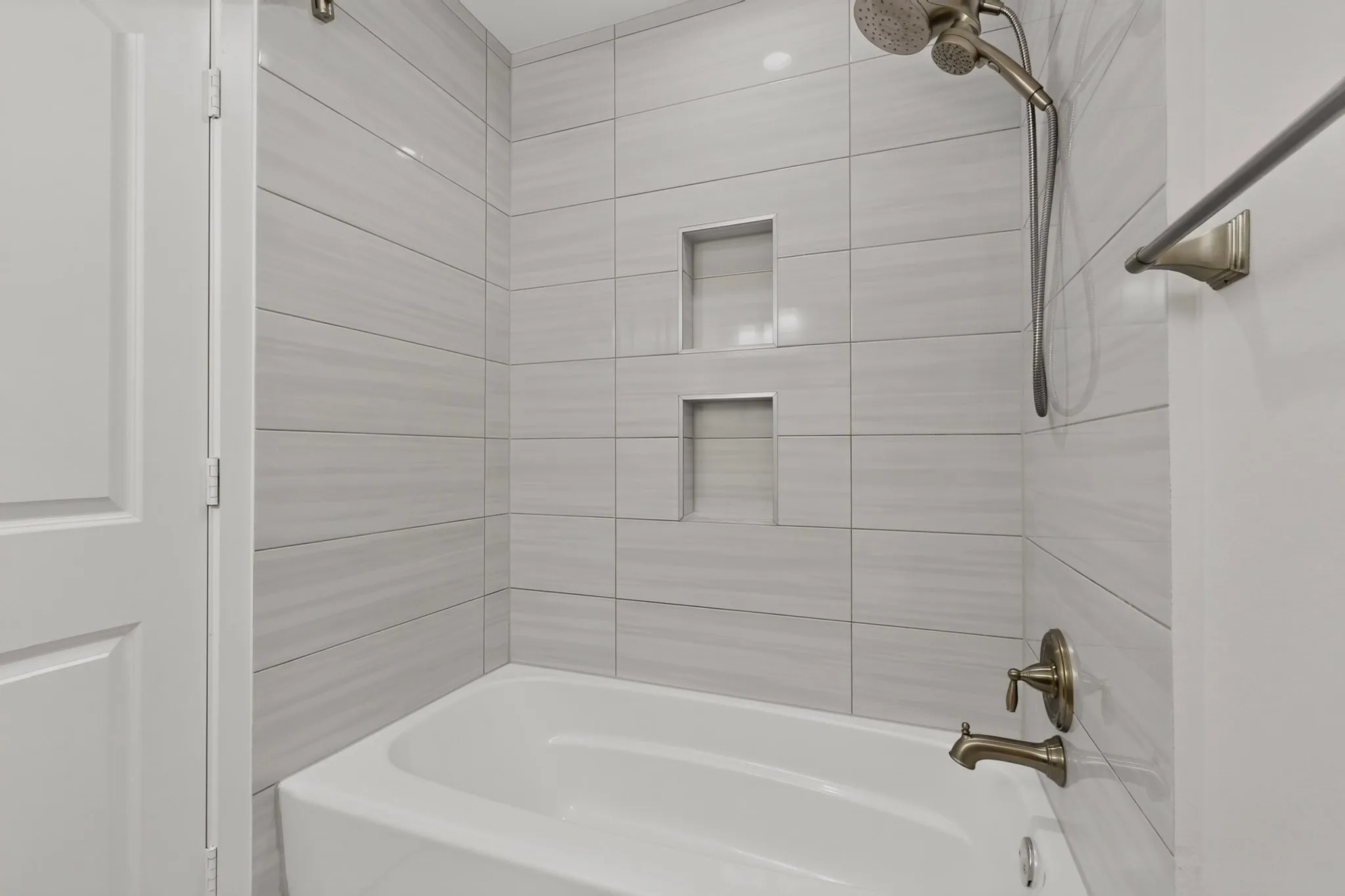 Modern bathroom featuring horizontal tile walls, a frameless glass shower enclosure, built-in shower niches, a soaking tub with deck-mounted faucet, and brushed nickel fixtures and hardware
