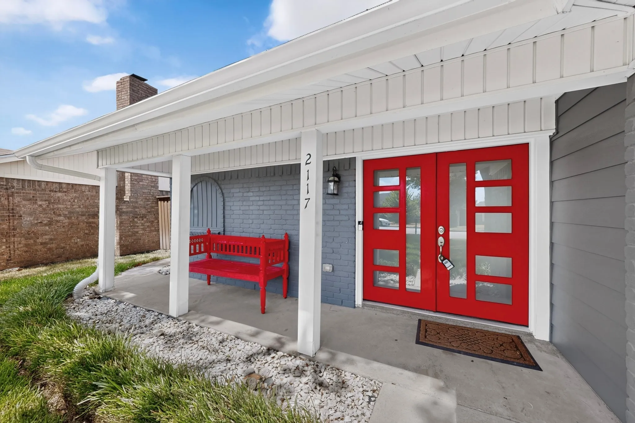 Covered front porch with white columns, red double entry doors with multiple lites, grey brick and siding exterior, and exterior wall lantern