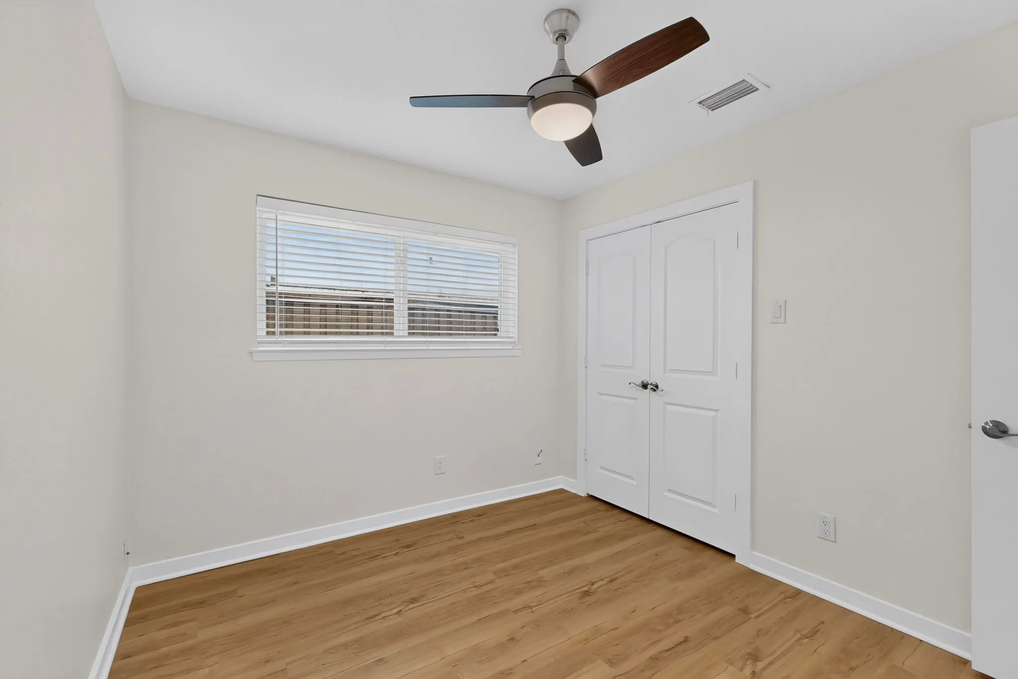 Recessed window with blinds, wood-finish flooring, and a modern ceiling fan with integrated lighting