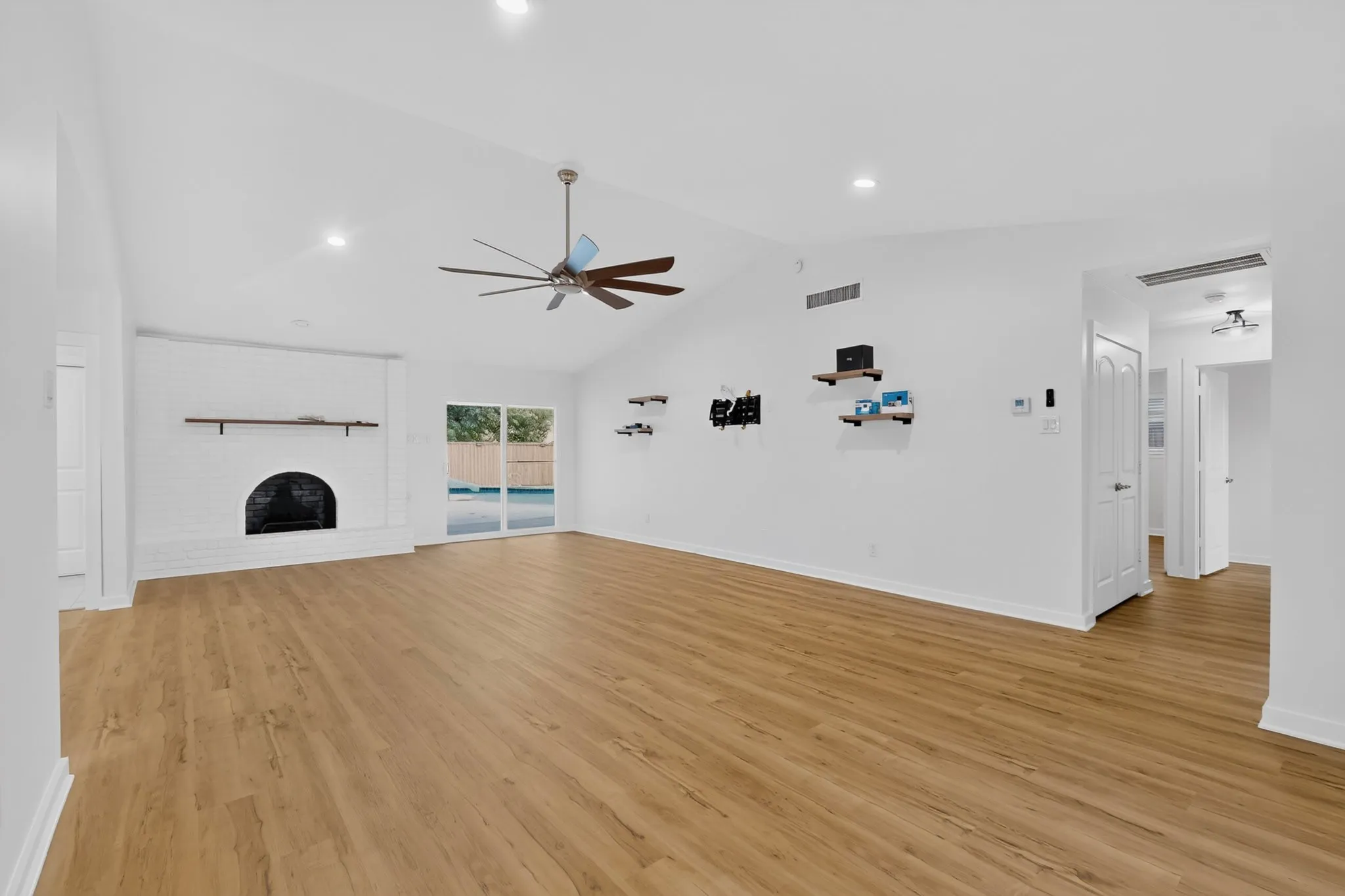 Vaulted ceiling, wood-finish flooring, white brick fireplace, sliding glass doors, and recessed lighting