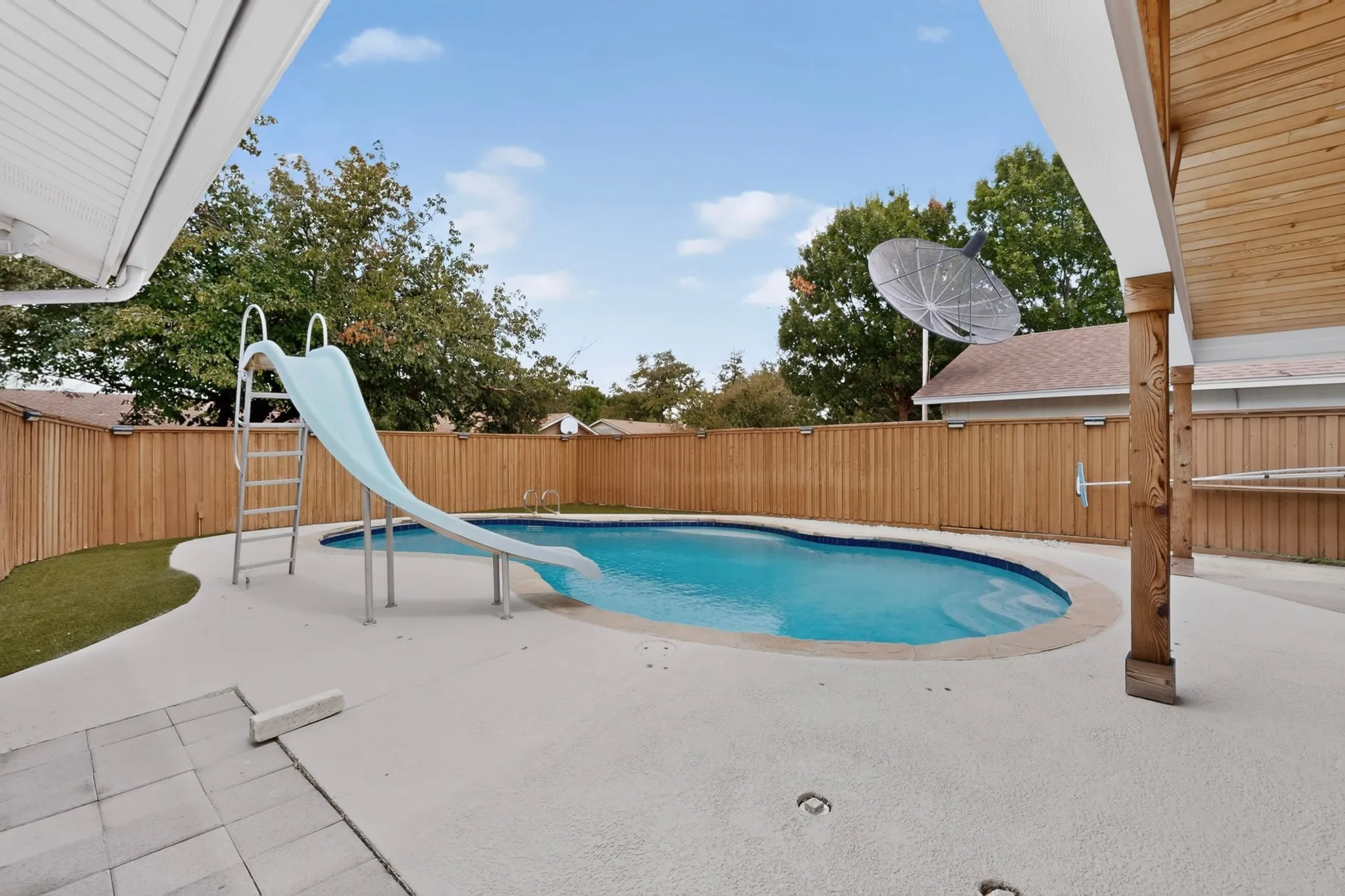 Outdoor swimming pool with a slide, surrounded by a wood privacy fence, concrete patio, and artificial turf