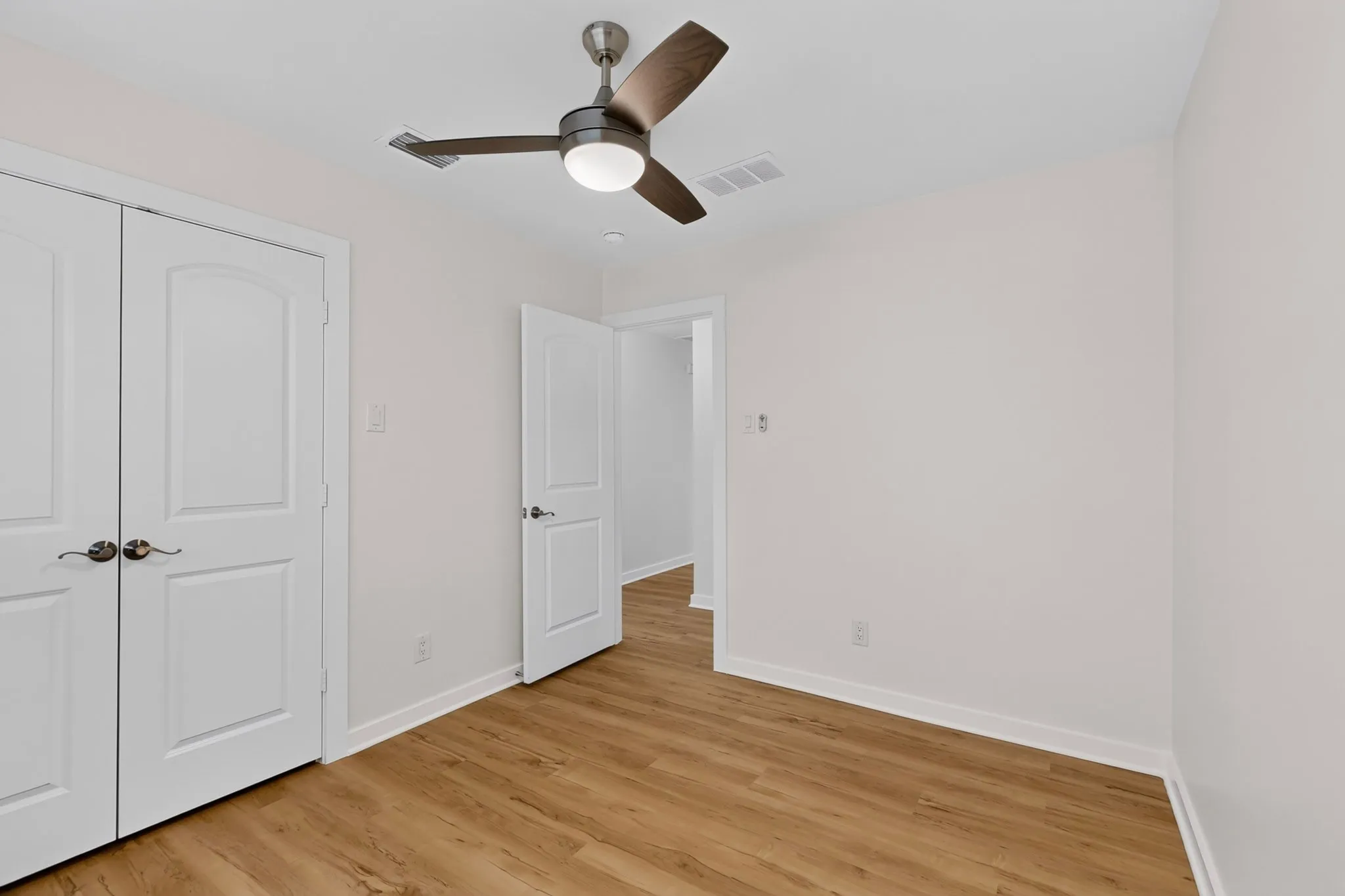 Wood-finish flooring, white walls, and a contemporary ceiling fan with integrated lighting
