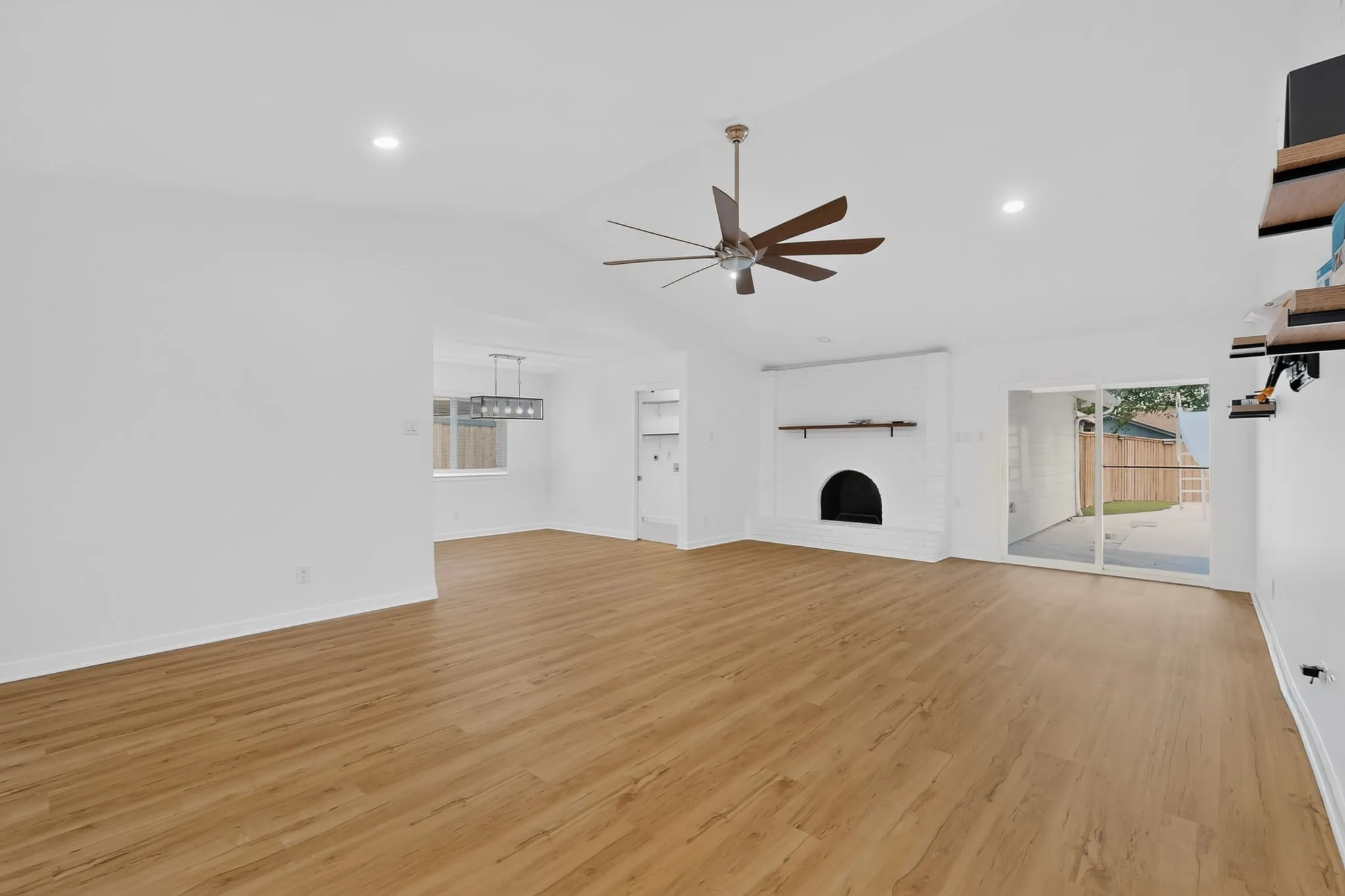 Vaulted ceiling with recessed lighting, wood-finish flooring, white brick fireplace with mantel, ceiling fan, and sliding glass door to outdoor patio