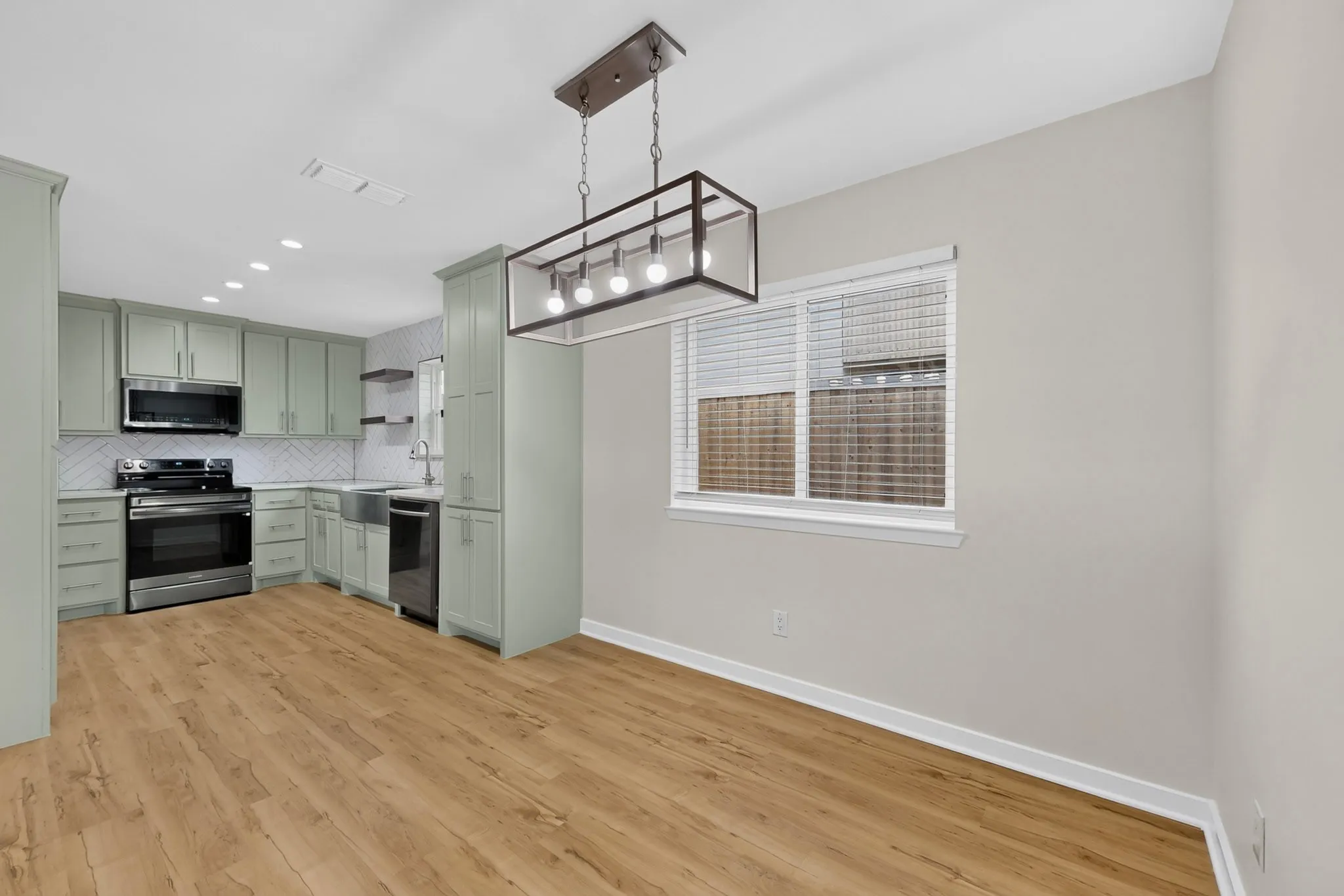 Spacious kitchen with wood-finish flooring, light green cabinetry, stainless steel appliances, and a tile backsplash