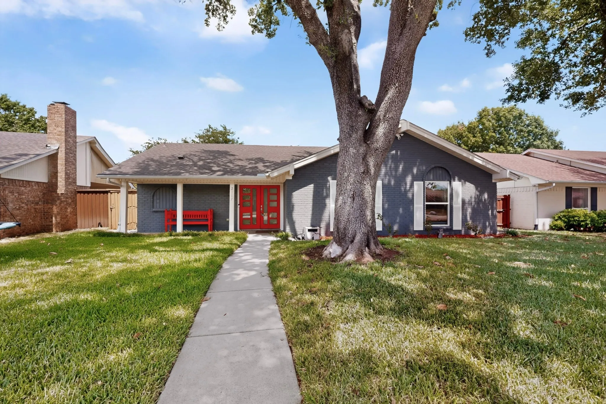 Single-story residence featuring a gray exterior, red double entry doors, a covered front porch, and a mature tree in the front yard