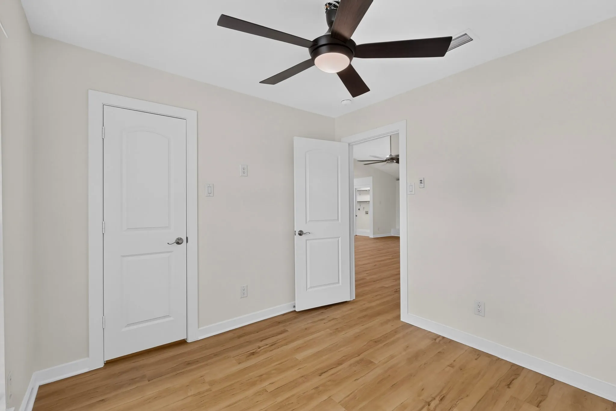 Wood-finish flooring, white walls, white trim, white panel doors, and a ceiling fan with integrated lighting