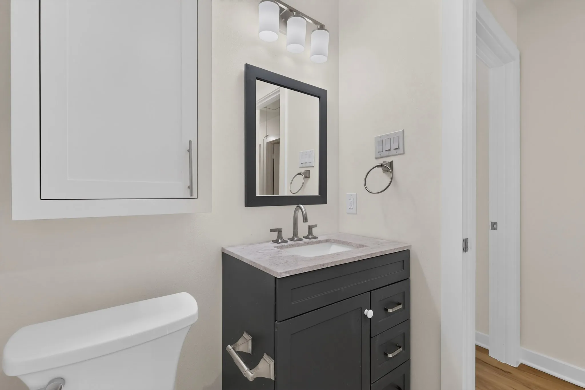 White recessed medicine cabinet, dark wood-finish vanity with a stone countertop and undermount sink, and a framed mirror with a three-light fixture
