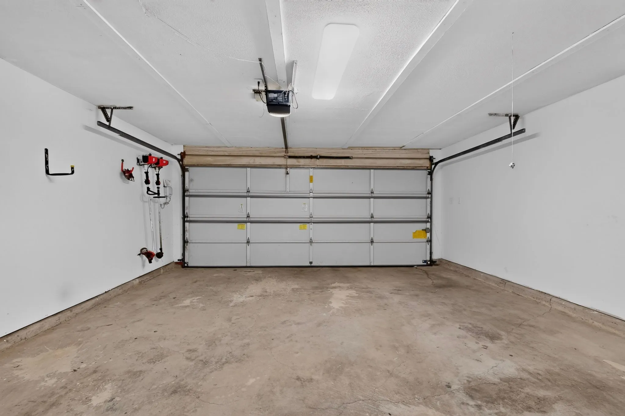 Spacious garage interior featuring concrete flooring, overhead garage door with panel design, automatic door opener system, and wall-mounted storage hardware