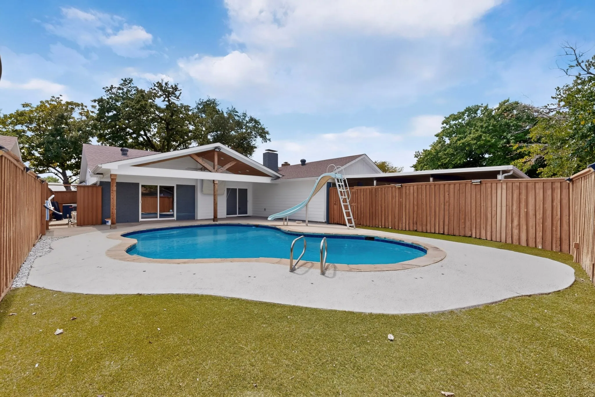 Backyard featuring a freeform swimming pool, concrete pool deck, artificial turf, and wood privacy fencing