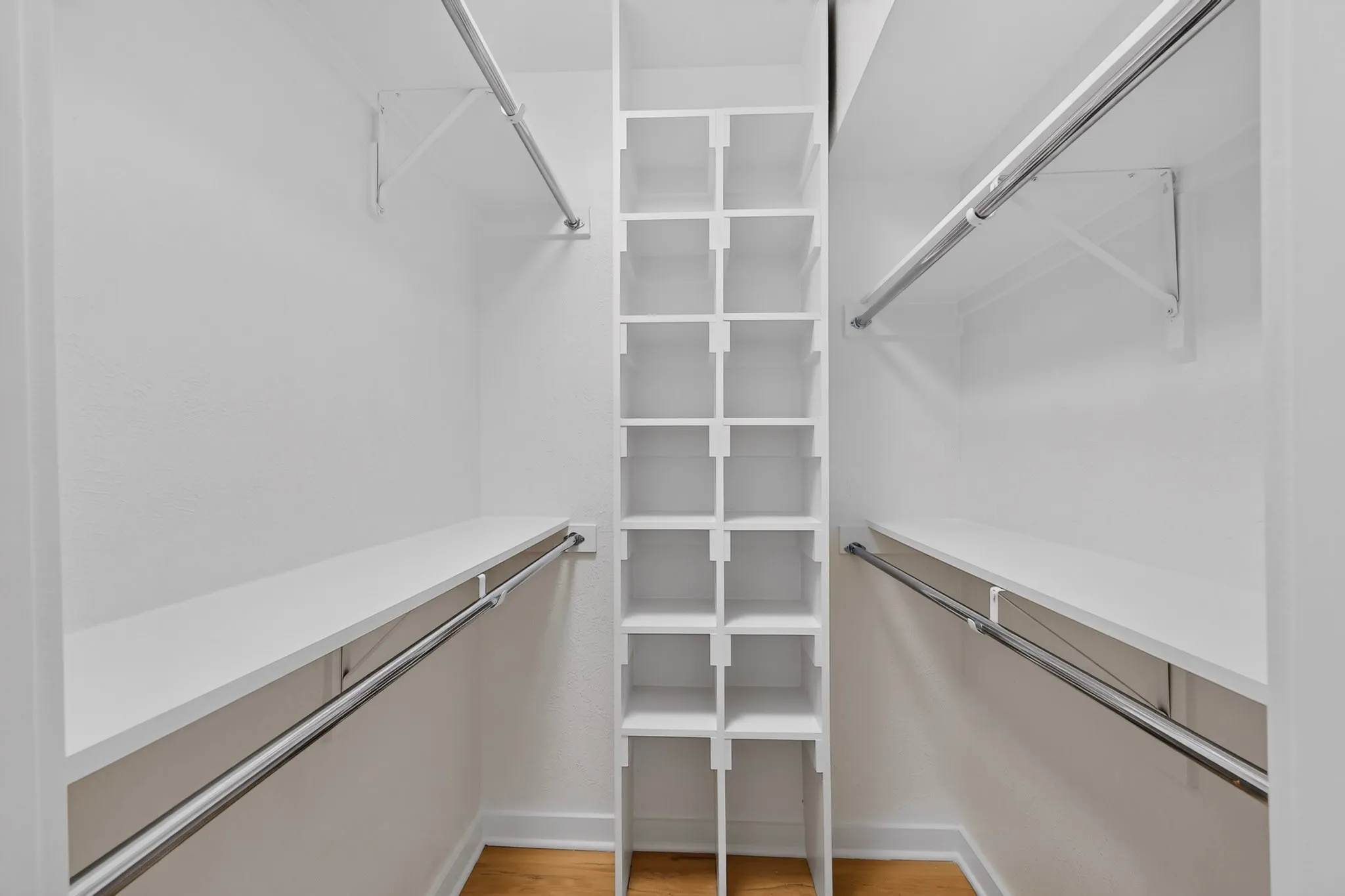 Walk-in closet featuring built-in shelving, multiple hanging rods, and wood-finish flooring