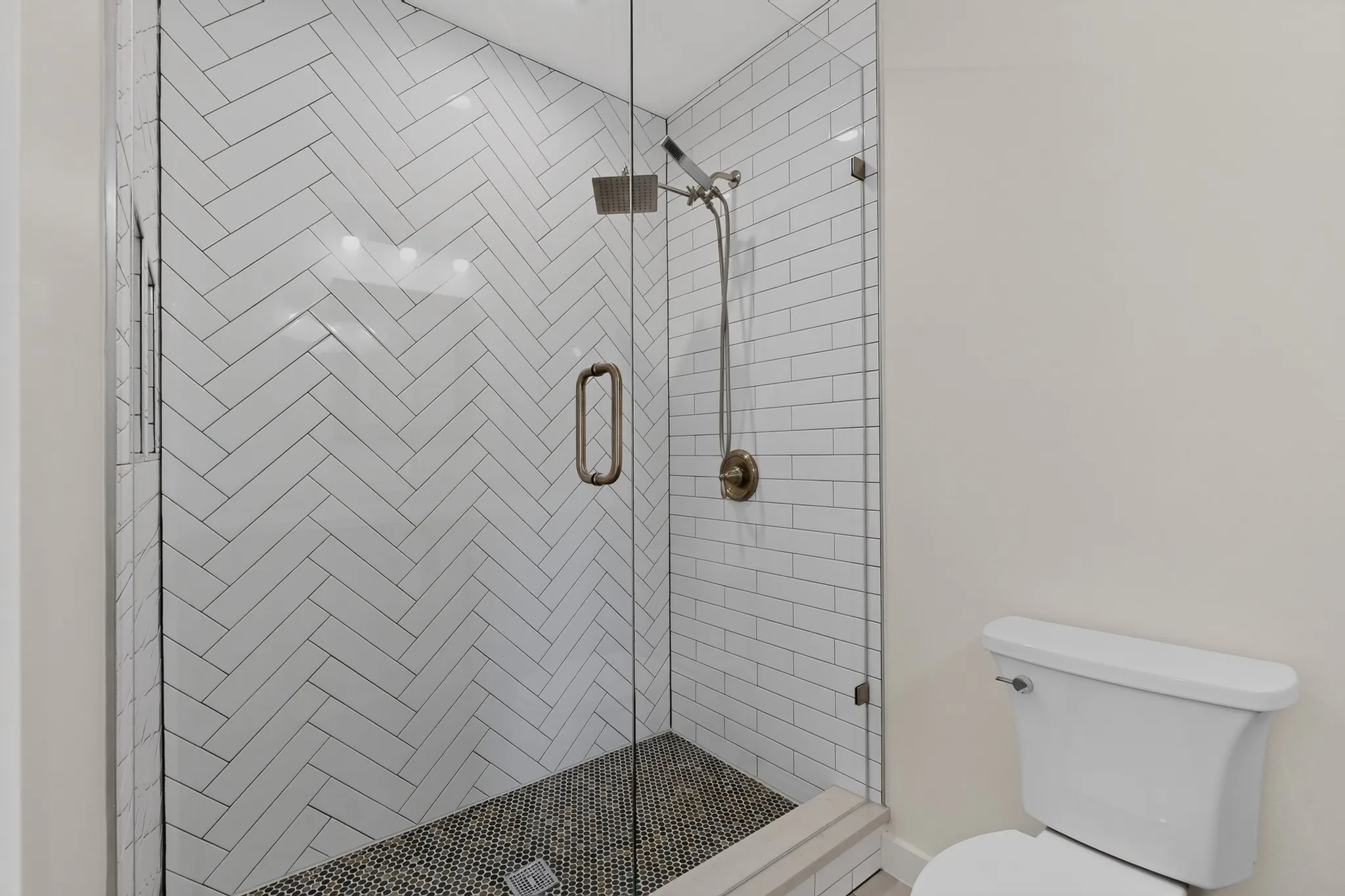 Glass-enclosed shower with a herringbone tile pattern, mosaic tile shower floor, and a built-in shower niche