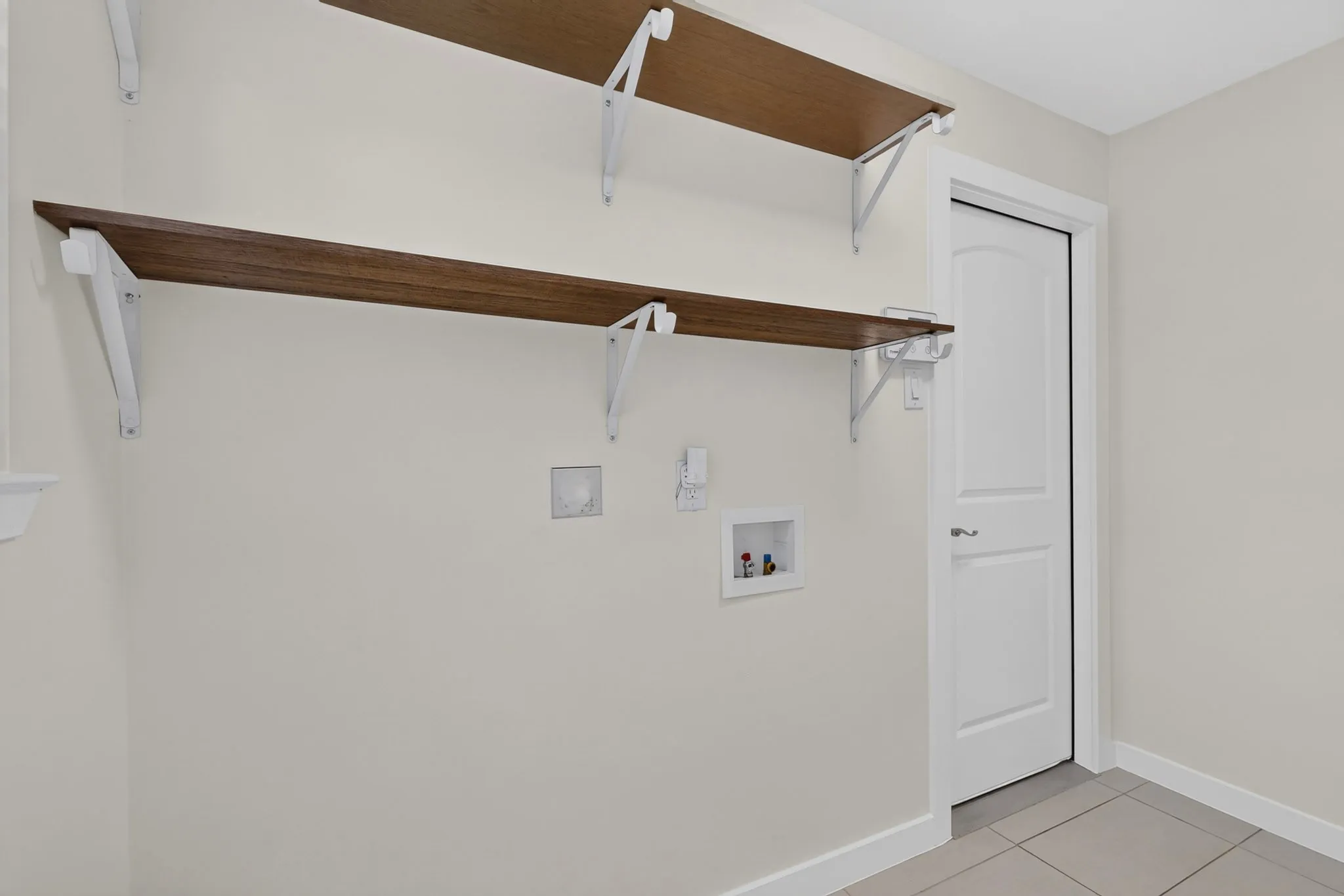 Recessed utility connections, dual wood-finish shelving, and light-toned tile flooring