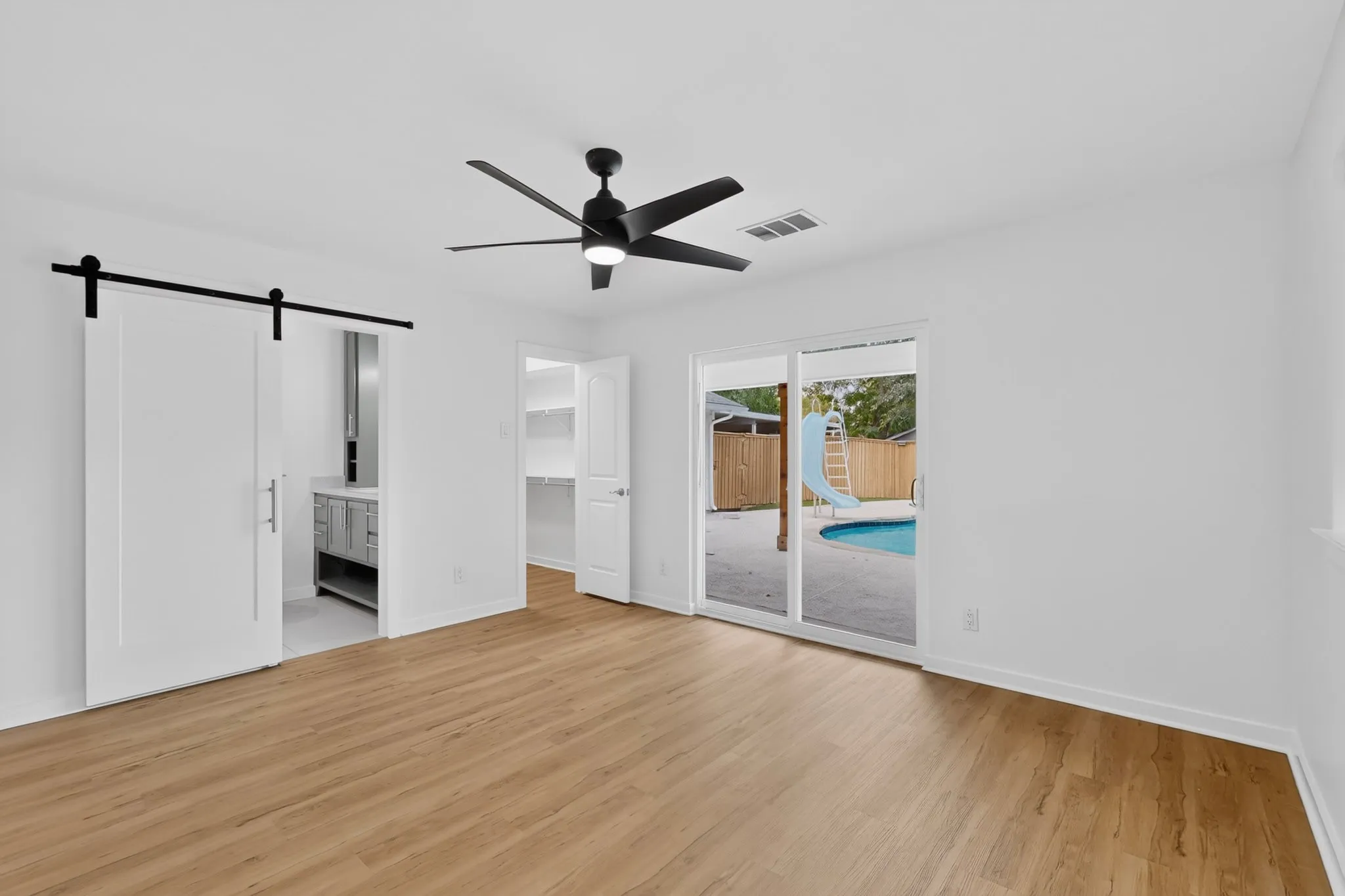 Wood-finish flooring, modern ceiling fan, sliding barn door, walk-in closet with shelving, and sliding glass door to exterior