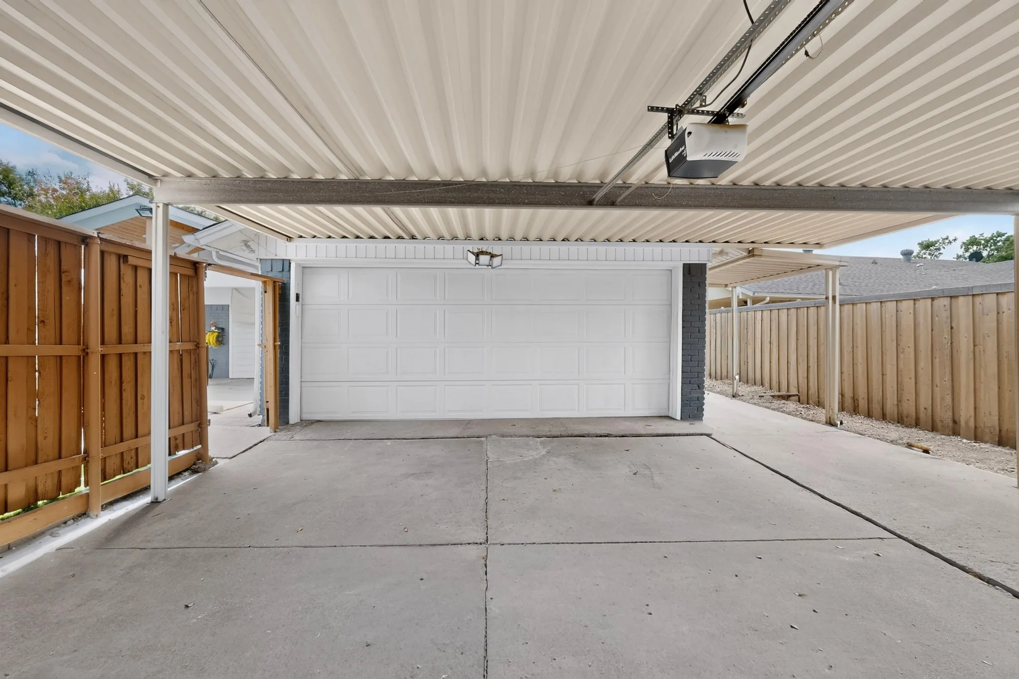 Covered parking structure with an automatic garage door, concrete driveway, and wood privacy fencing