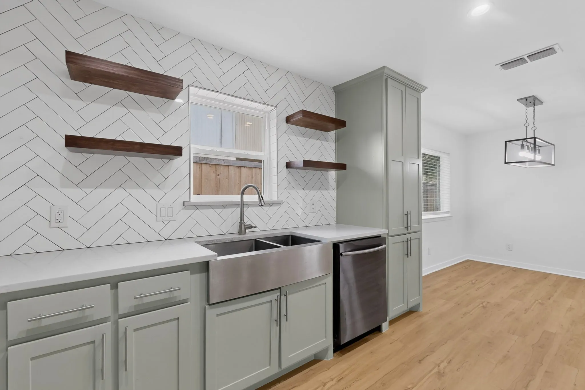 Kitchen featuring a subway tile backsplash in a herringbone pattern, stainless steel farmhouse sink, light green cabinetry, white countertops, and wood-finish flooring