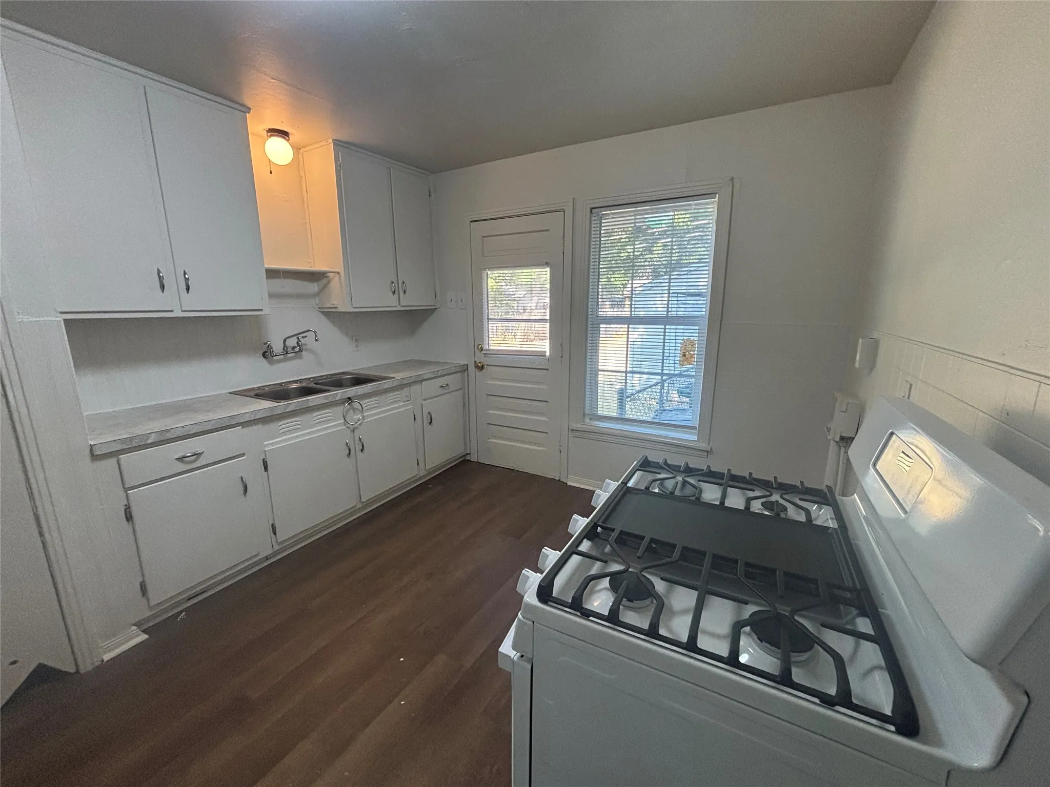 Kitchen featuring white cabinetry, dual-basin stainless steel sink, wood-finish flooring, and a gas range