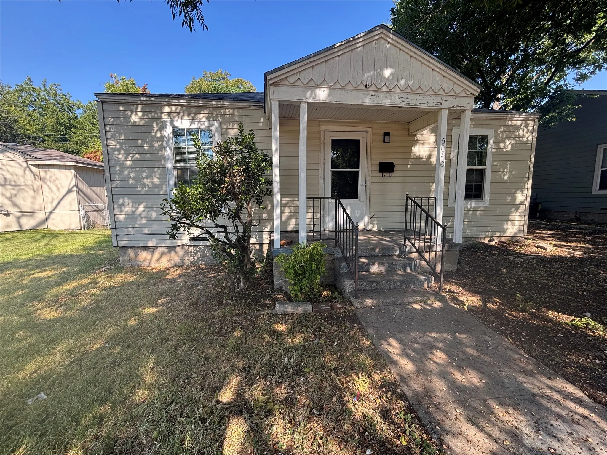 Siding exterior with a covered front porch featuring decorative trim, black metal railings, and a concrete pathway