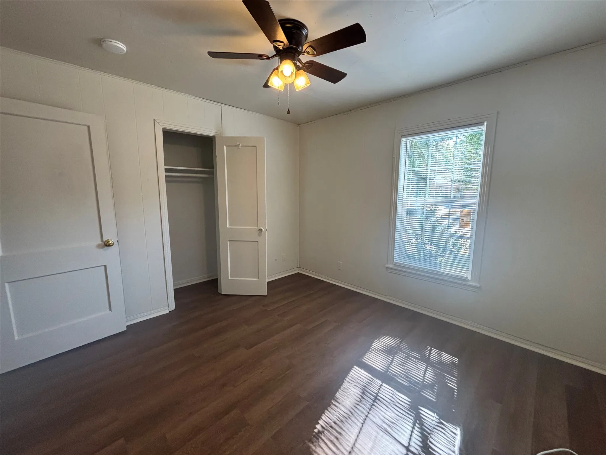 Wood-finish flooring with white baseboards, a ceiling fan with integrated lighting, and a window with blinds