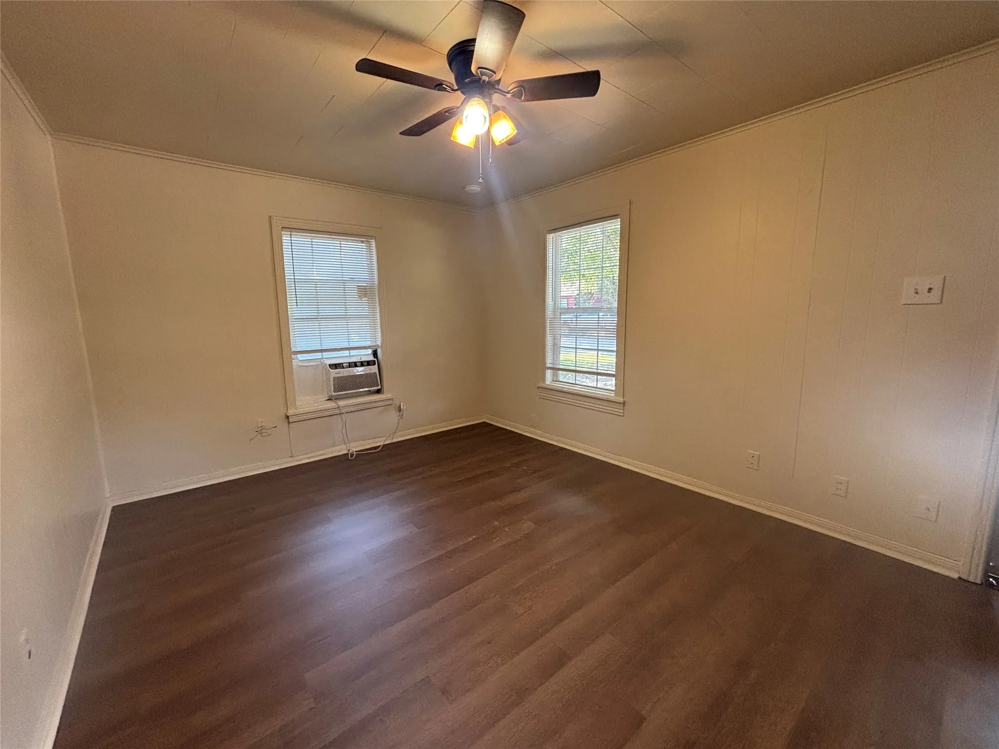 Wood-finish flooring, two windows with blinds, ceiling fan with integrated lighting, and crown molding