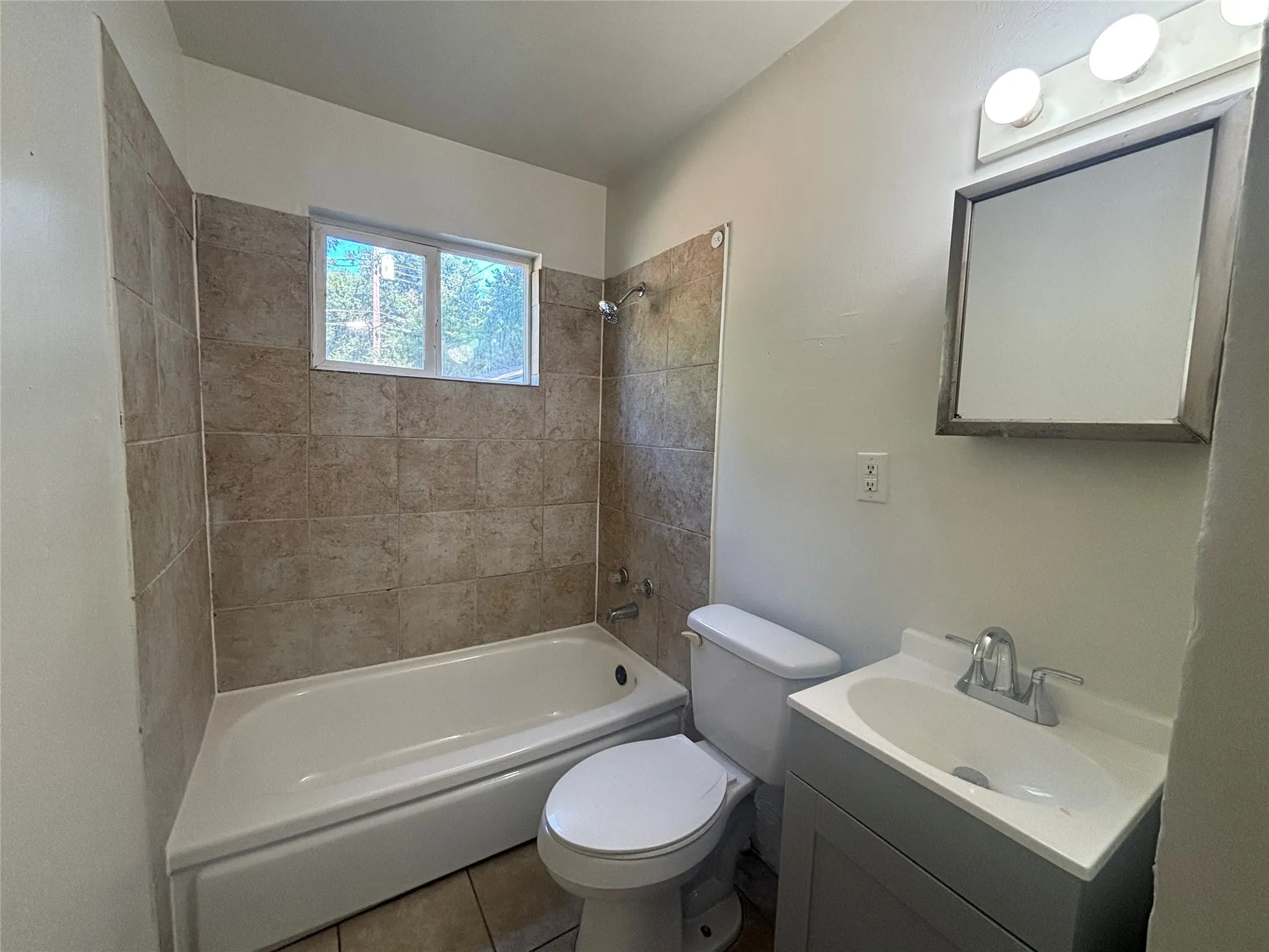 Bathroom featuring a white bathtub, ceramic tile surround, window, single vanity with integrated sink, and wall-mounted mirror
