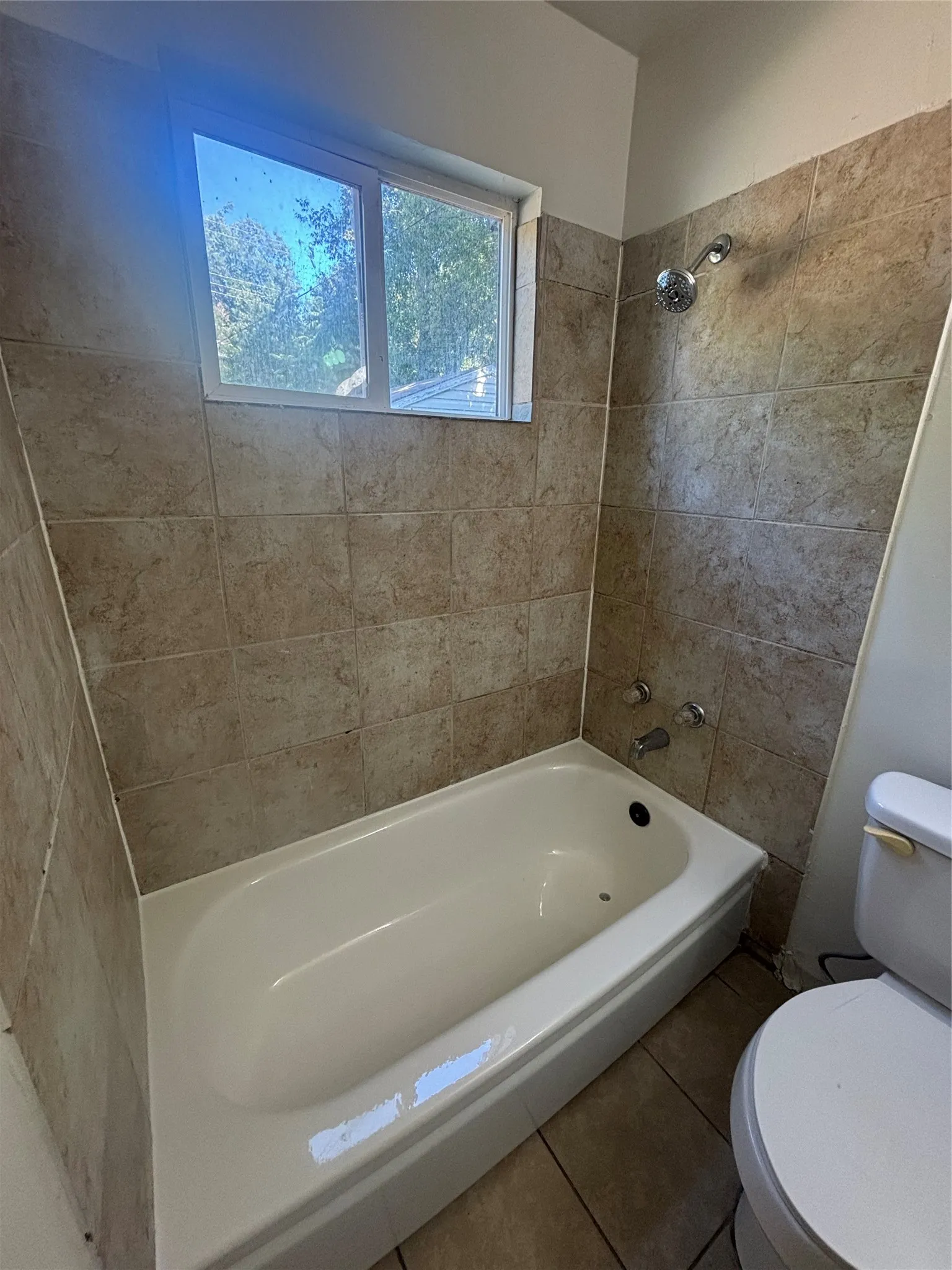 Tiled shower and bathtub combination with a window, complete with a showerhead and tub fixtures