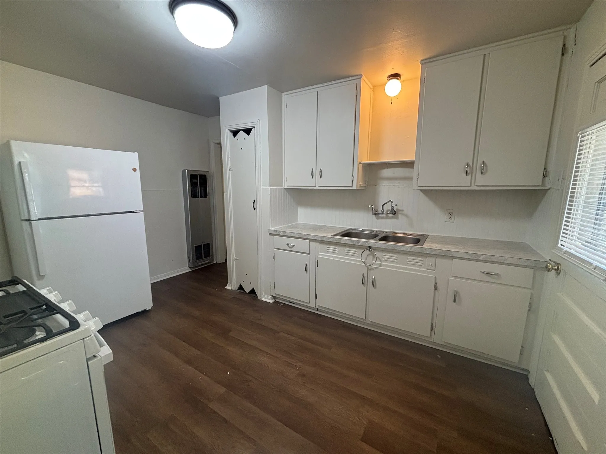 Kitchen with wood-finish flooring, white cabinetry, double basin sink, and a white gas range