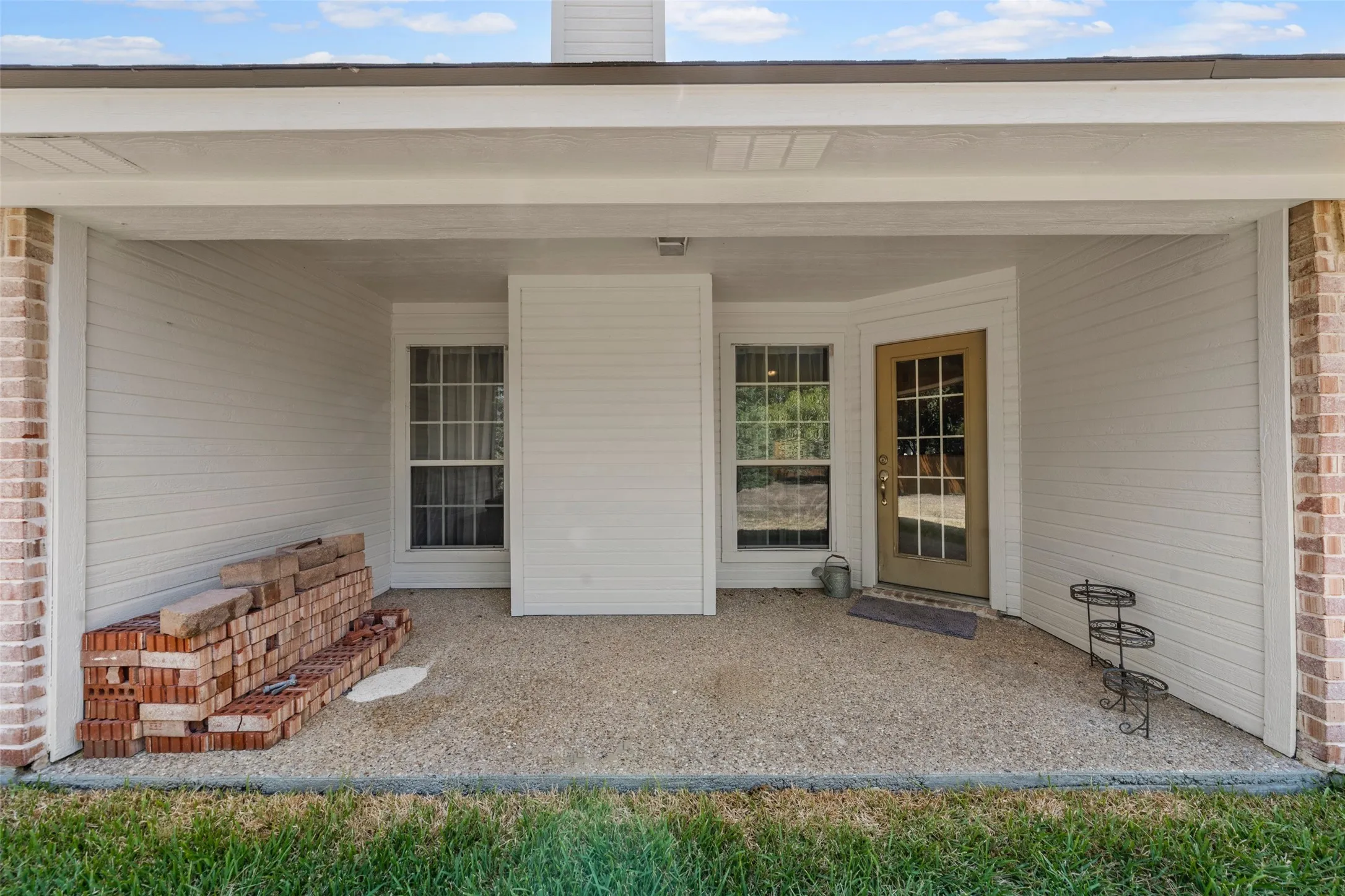 Covered patio with an exposed aggregate concrete surface, white siding, and brick columns