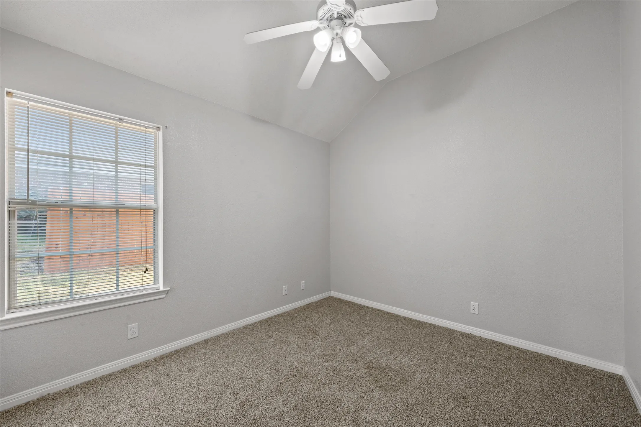 Vaulted ceiling, ceiling fan with light fixture, neutral carpeting, window with blinds, and light gray wall finish