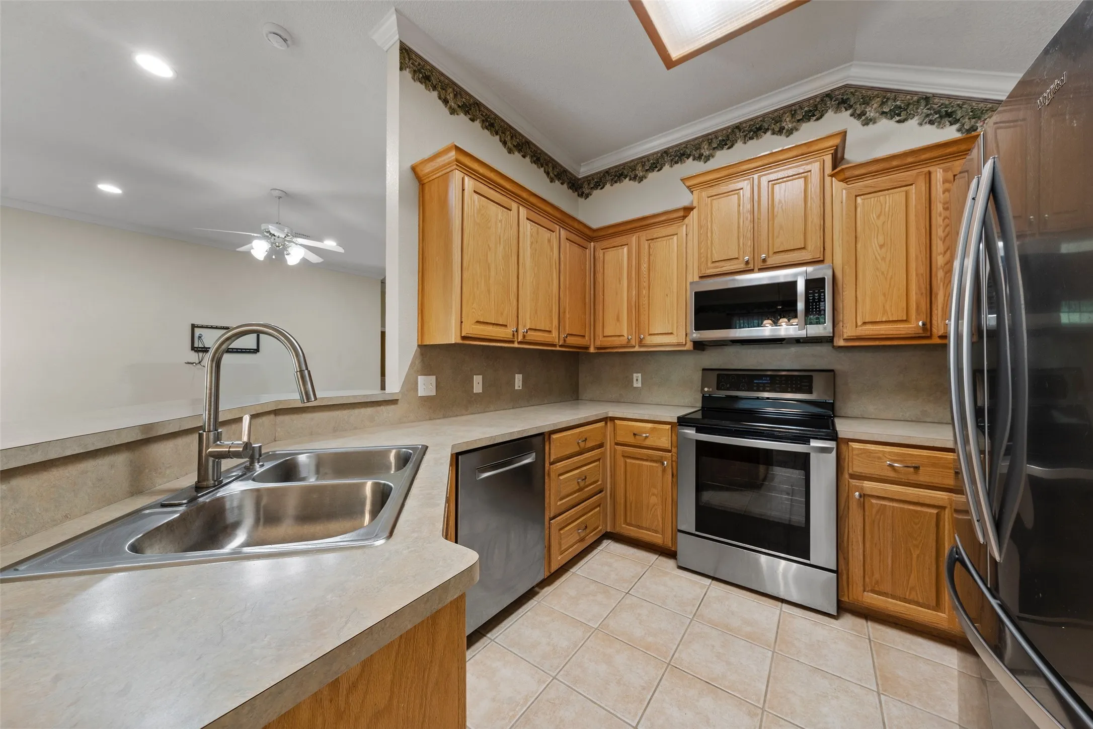 Kitchen featuring wood cabinetry, stainless steel appliances, a double basin sink, and tile flooring