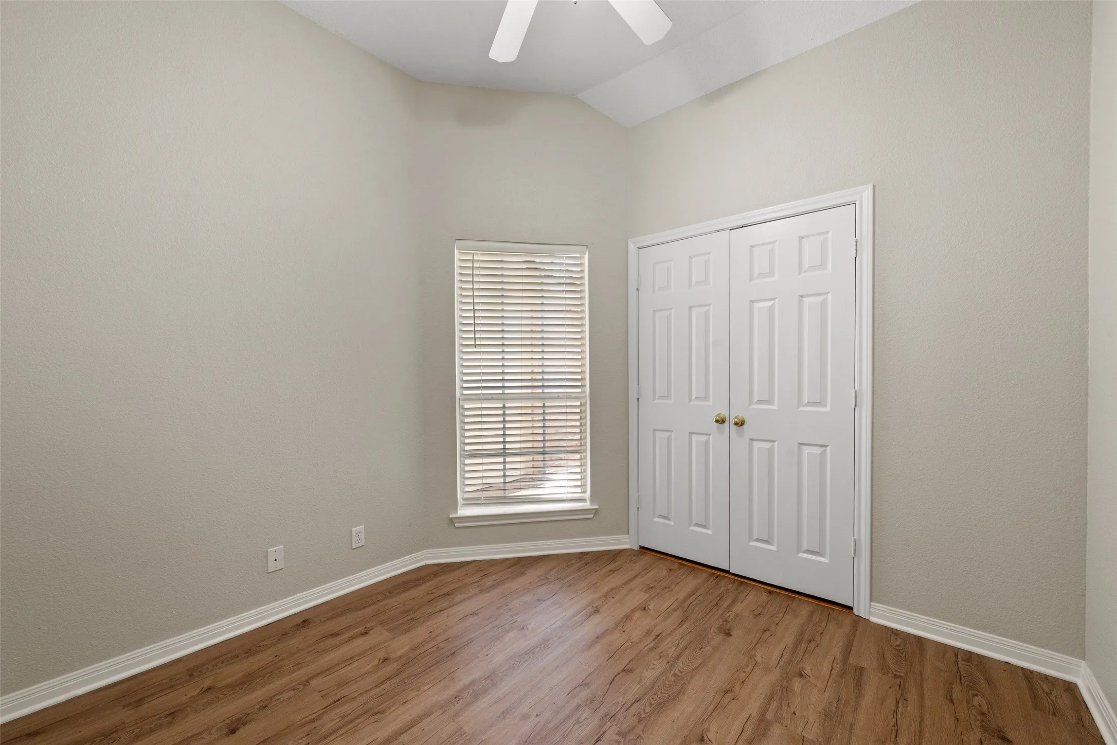Vaulted ceiling, wood-finish flooring, window with horizontal blinds, ceiling fan, and bi-fold closet doors