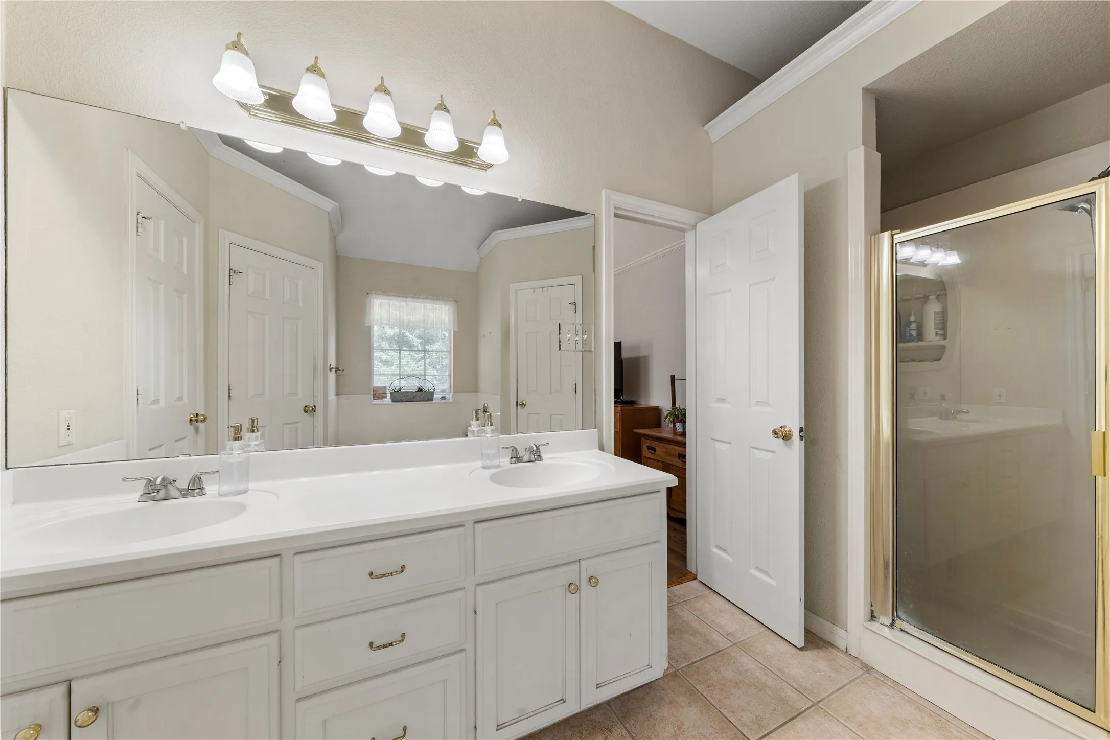 Dual vanity with integrated sinks, expansive mirror, polished chrome fixtures, white cabinetry, and a shower enclosure