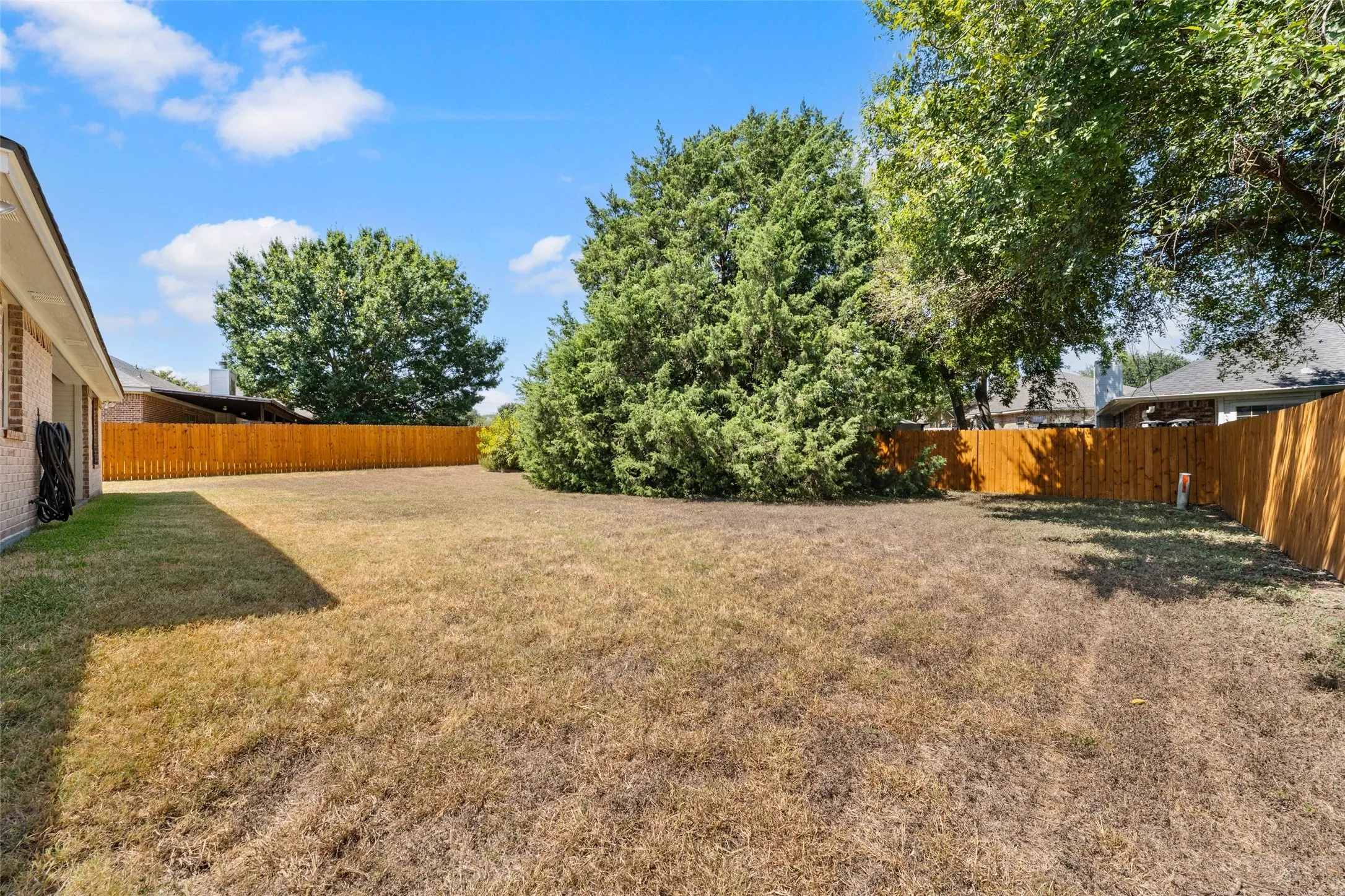 Expansive backyard featuring a wood fence, mature trees, and a brick exterior