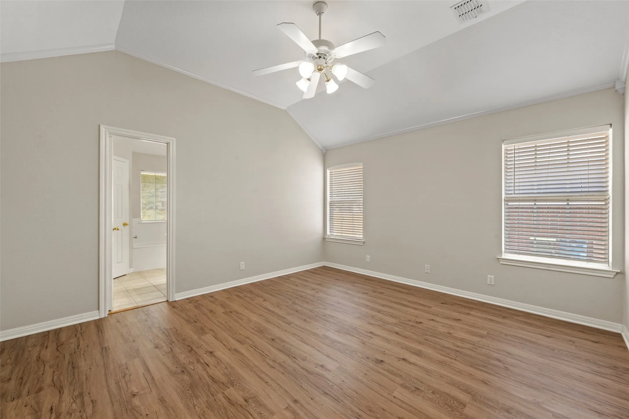 Vaulted ceiling with a ceiling fan, wood-finish flooring, and two windows with blinds