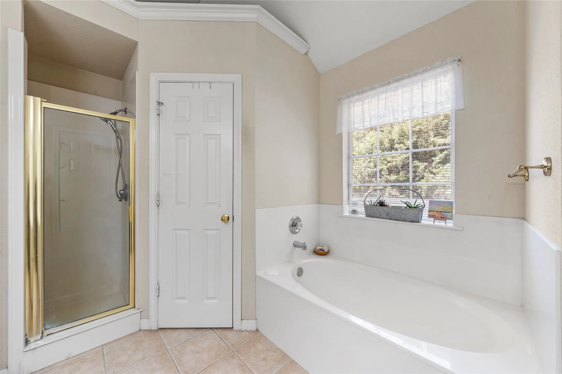 Built-in soaking tub with chrome fixtures, an adjacent shower enclosure with brass-finish framing, and tile flooring