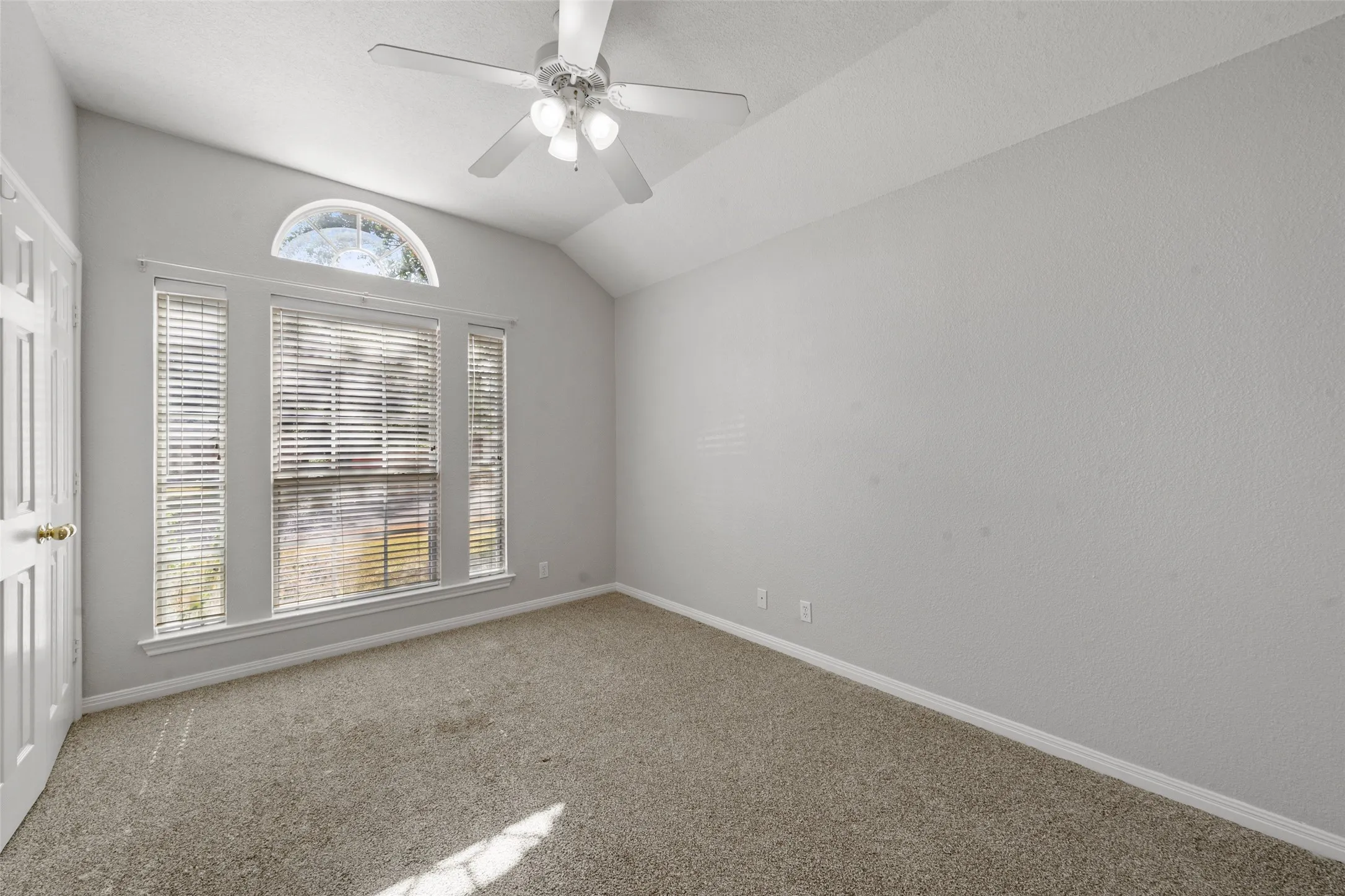 Vaulted ceiling with an attached ceiling fan, large window with blinds, and arched transom window