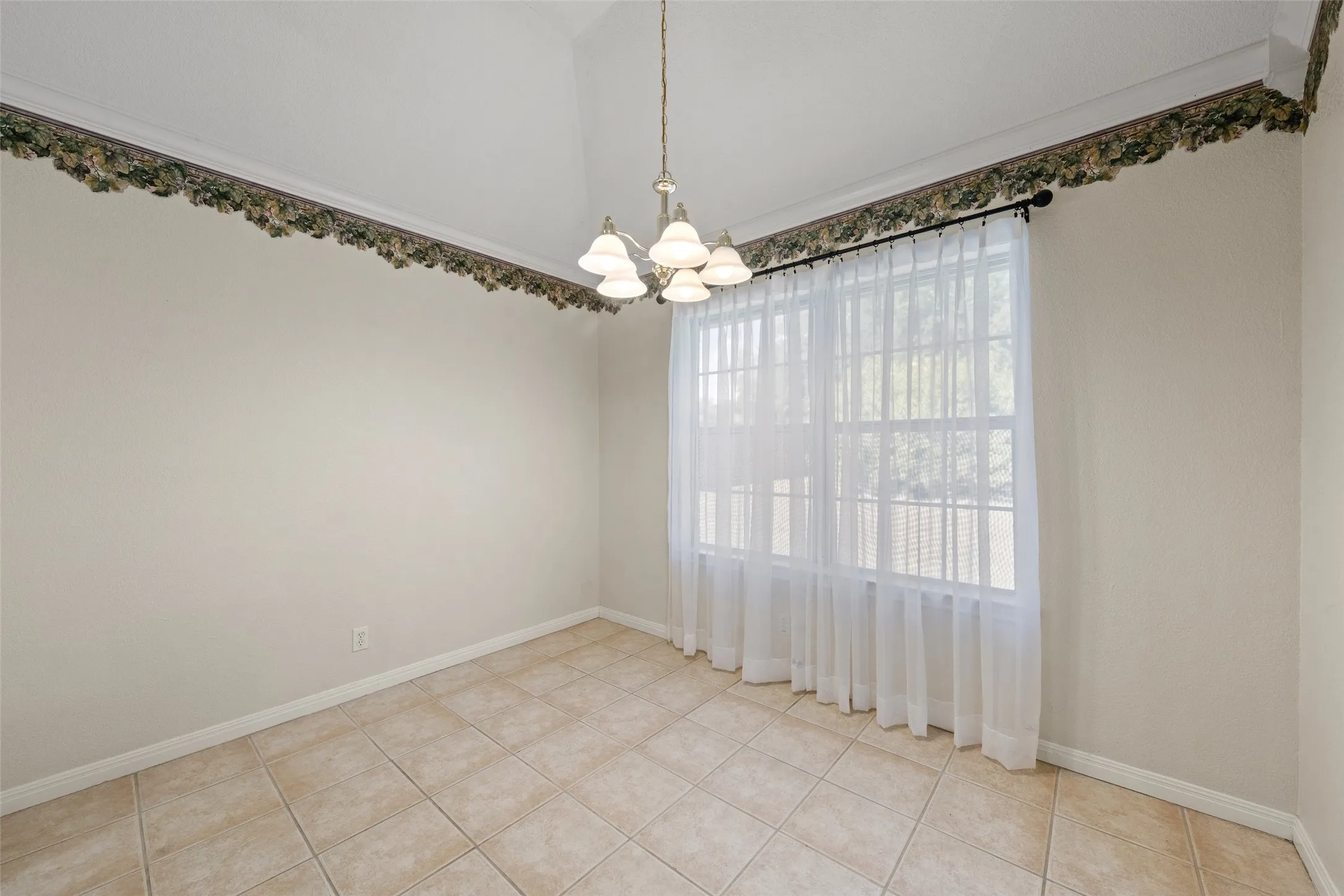 Vaulted ceiling with an attached chandelier, multiple windows, and tile flooring