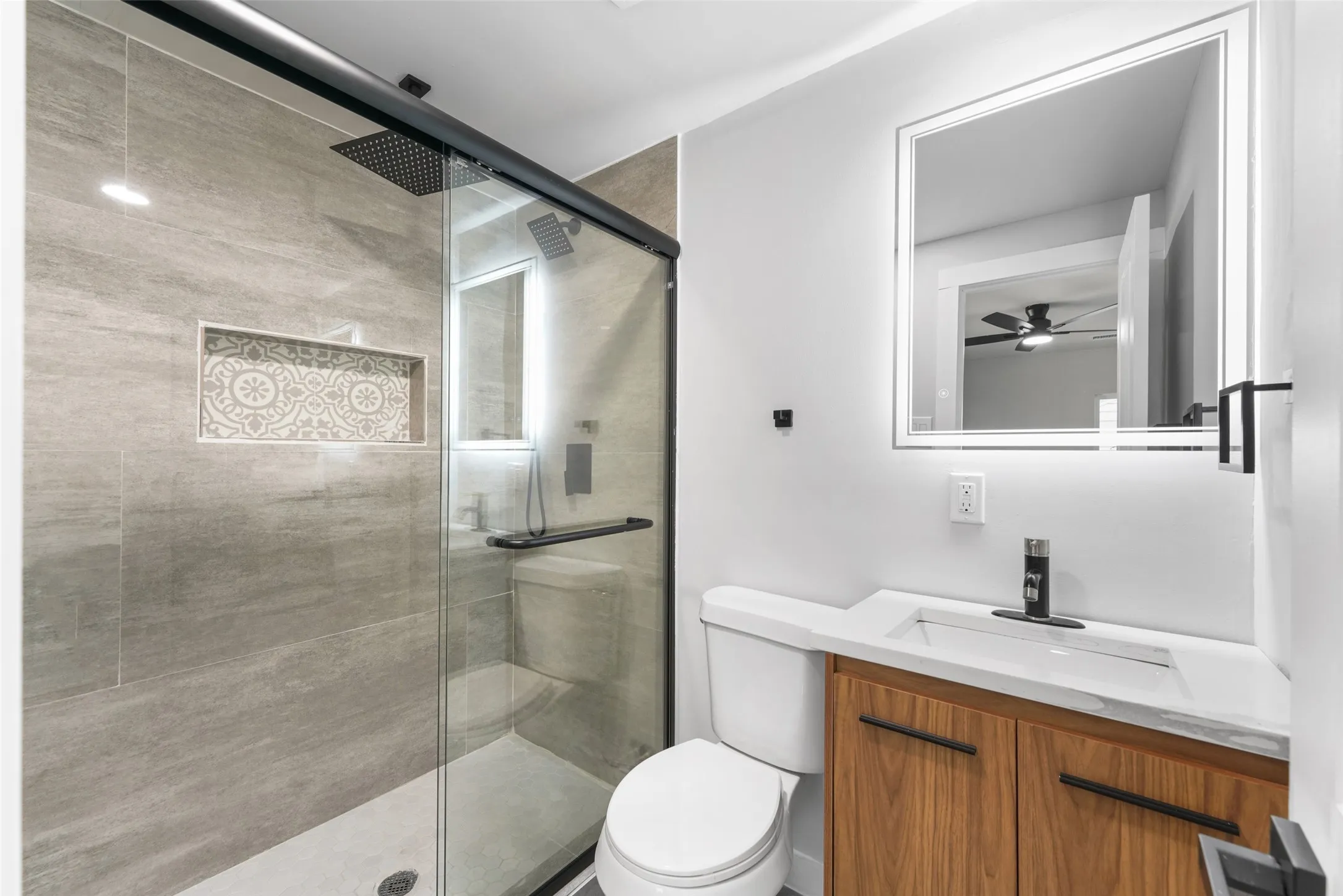 Glass-enclosed shower with a rainfall showerhead and tiled niche