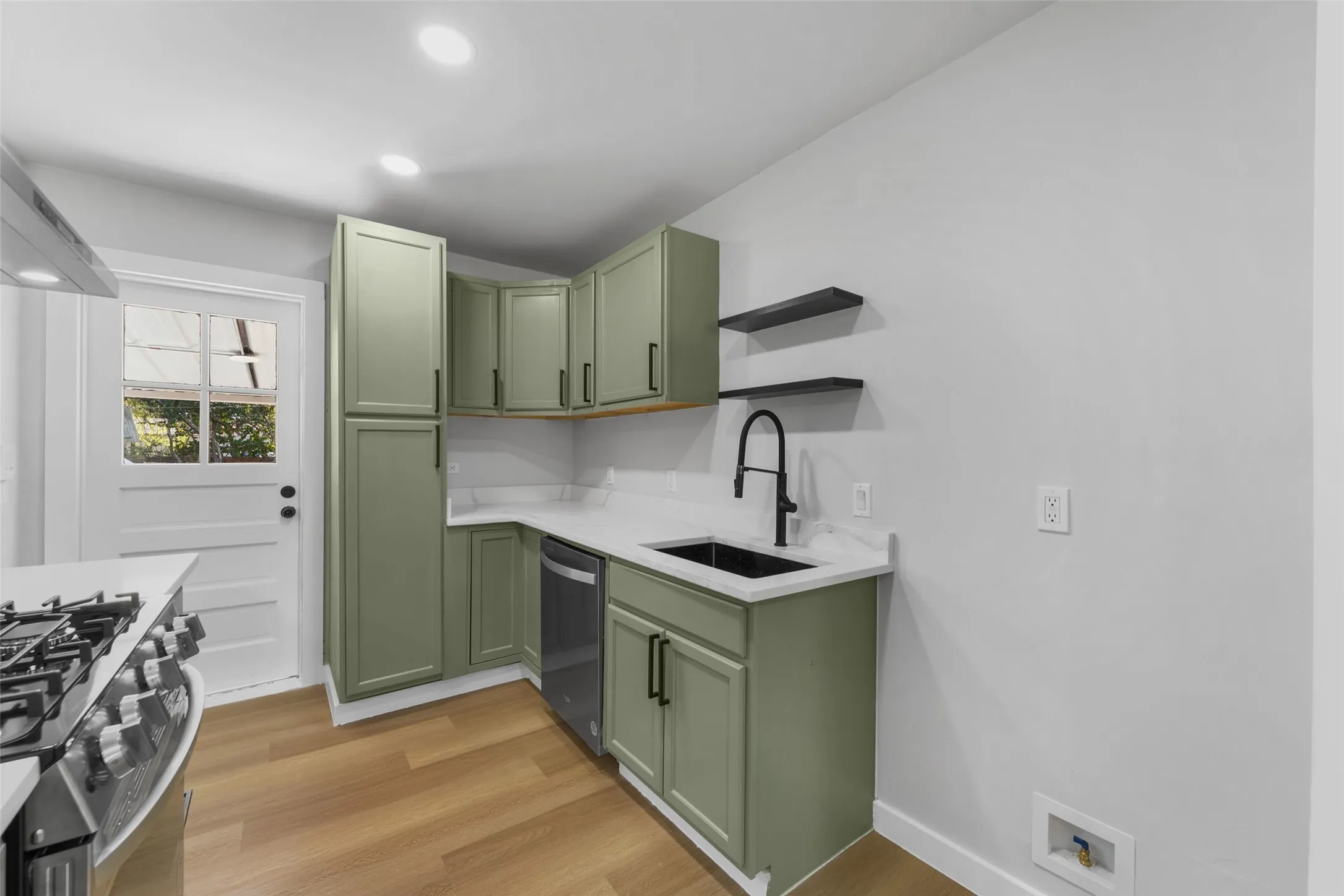 Kitchen featuring light wood-finish flooring, recessed lighting, sage green cabinetry with black hardware, white countertops, and a black sink with a matte black faucet