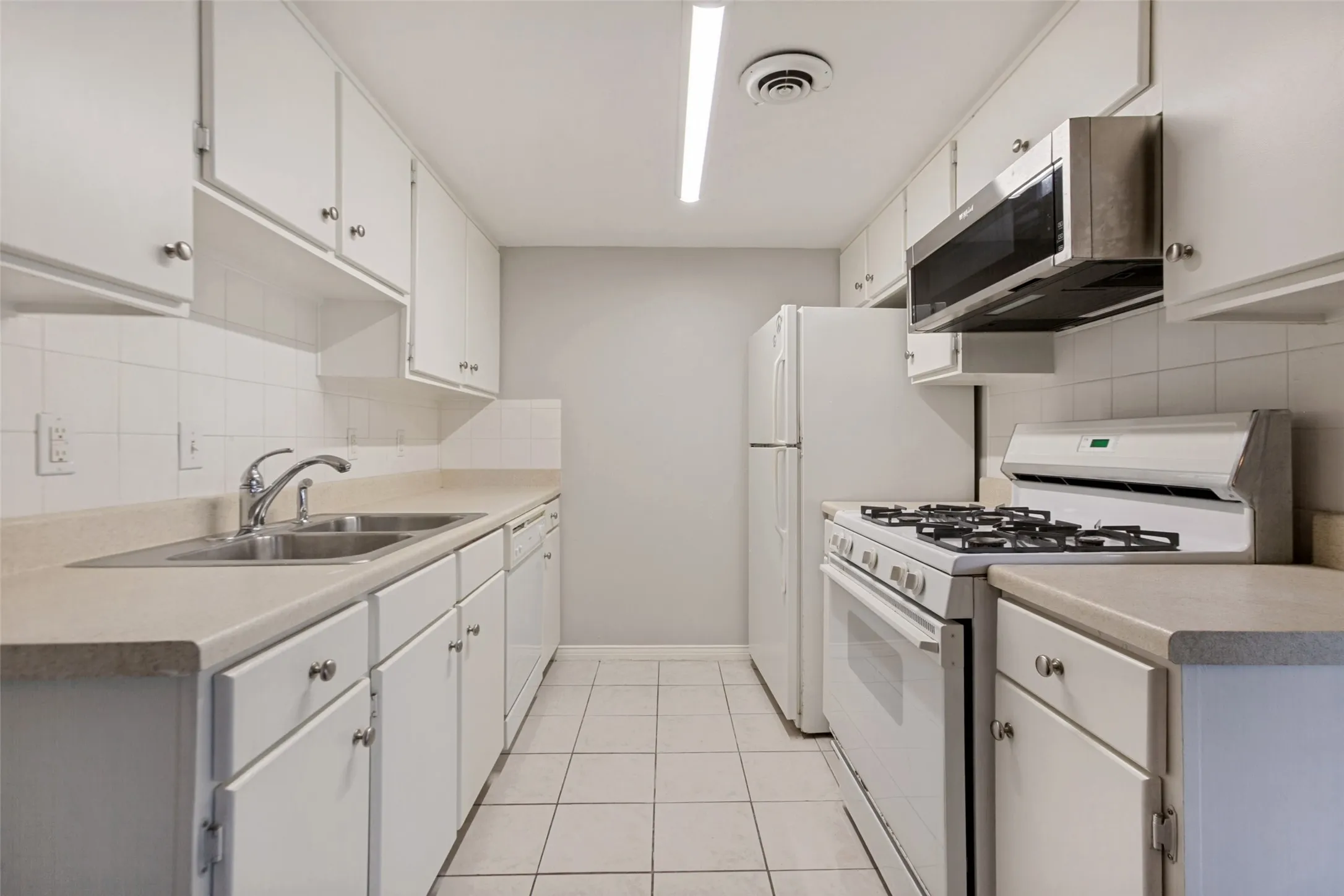 Galley kitchen with white cabinetry, tile flooring, and integrated white appliances