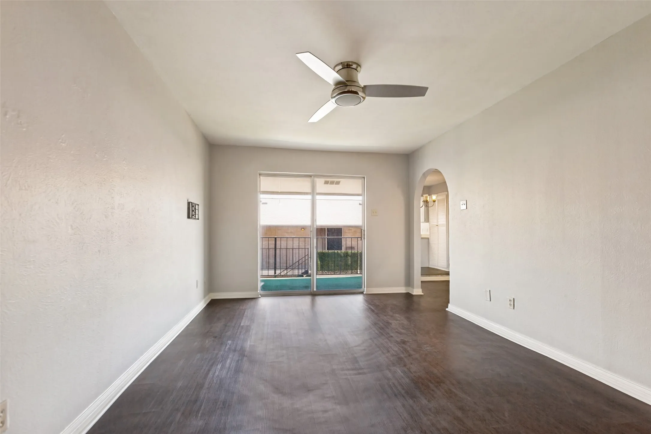 Dark wood-finish flooring, a ceiling fan with brushed nickel accents, and a sliding glass door to an outdoor area