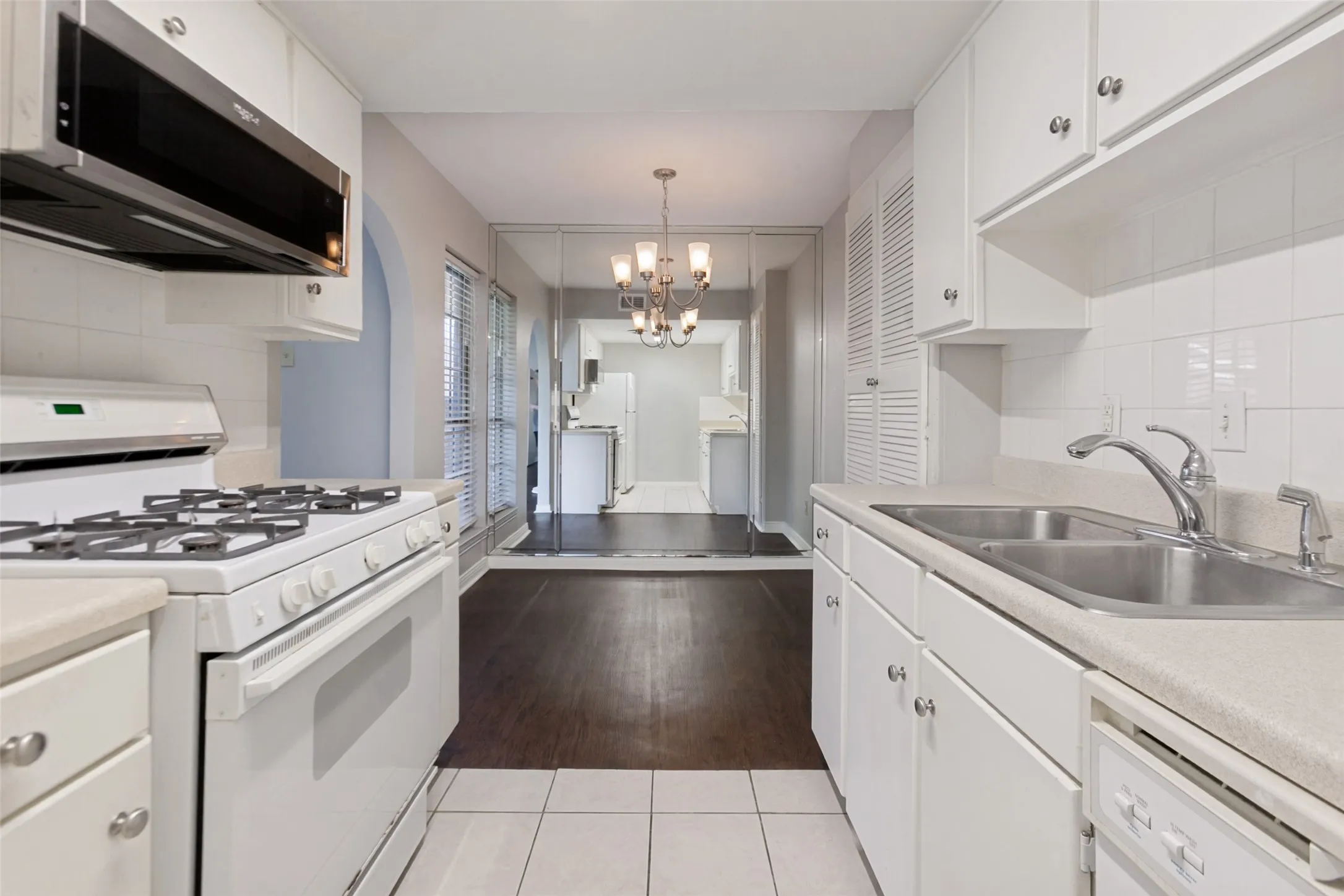 Kitchen with white cabinetry, tile backsplash, gas range, built-in microwave, and double basin sink