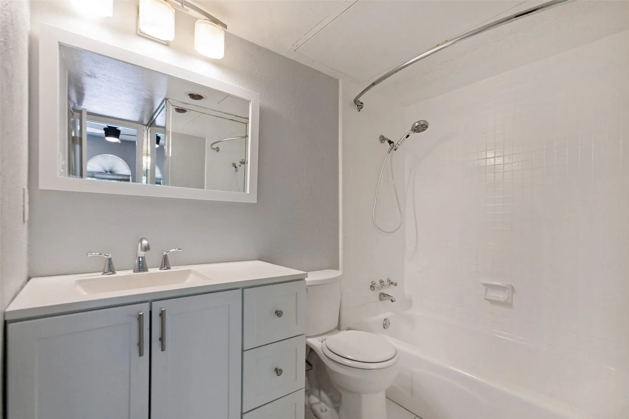Bathroom featuring a white vanity with integrated sink, chrome fixtures, framed mirror, and a white tiled shower/tub combination