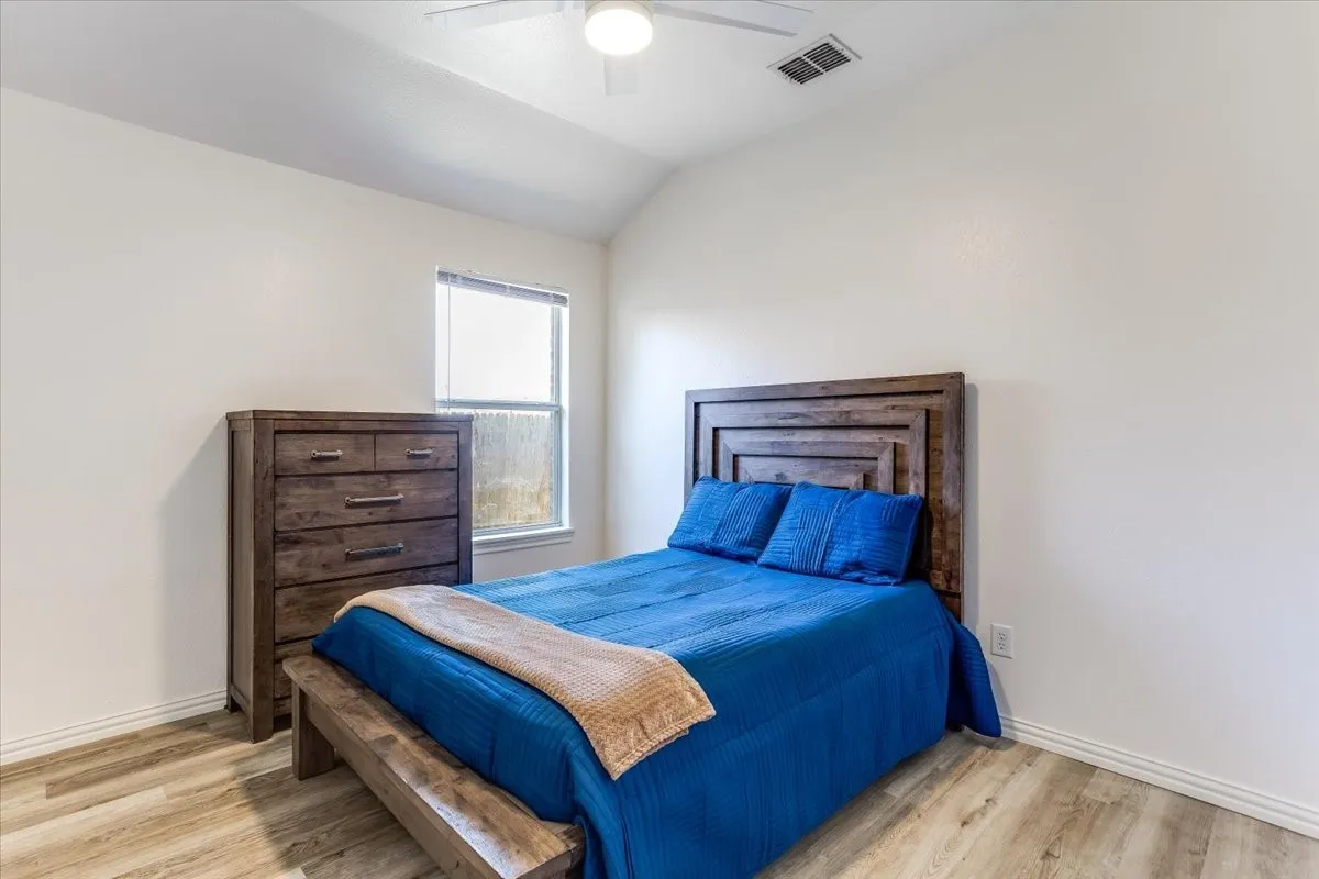 Vaulted ceiling with a ceiling fan, wood-finish flooring, and a window with blinds