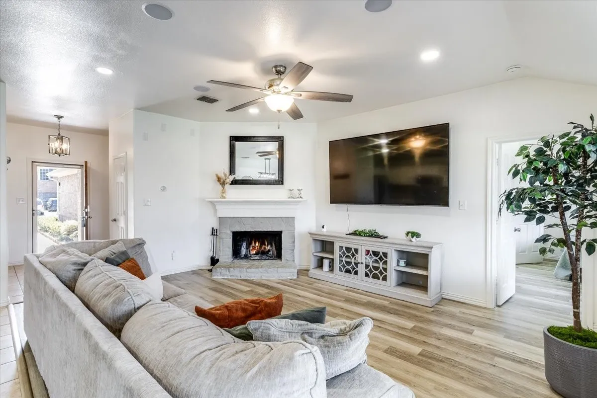 Living area featuring wood-finish flooring, a corner fireplace with a stone surround, and a ceiling fan