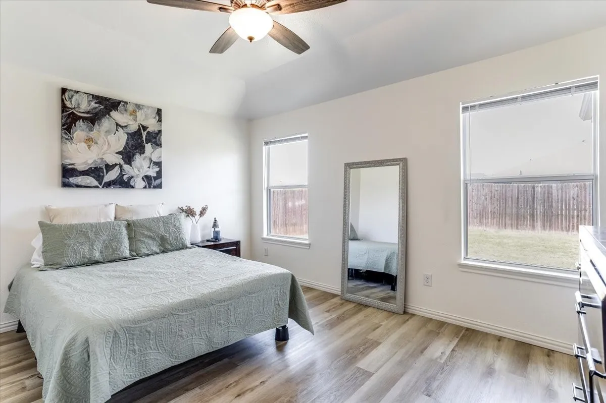 Vaulted ceiling featuring a ceiling fan, wood-finish flooring, and multiple windows with roller shades
