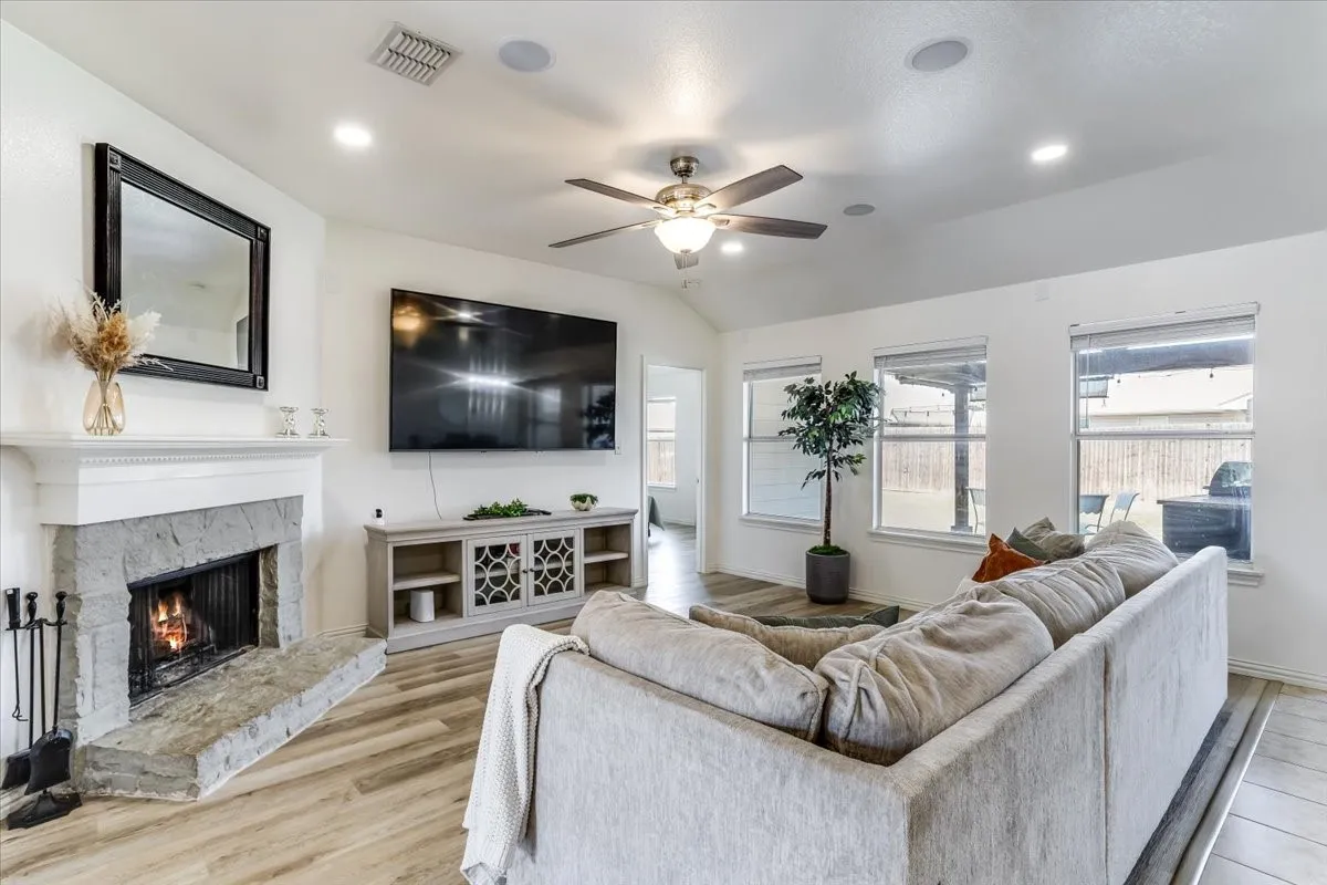 Vaulted ceiling with recessed lighting, stone fireplace with hearth, wood-finish flooring, ceiling fan, and multiple windows
