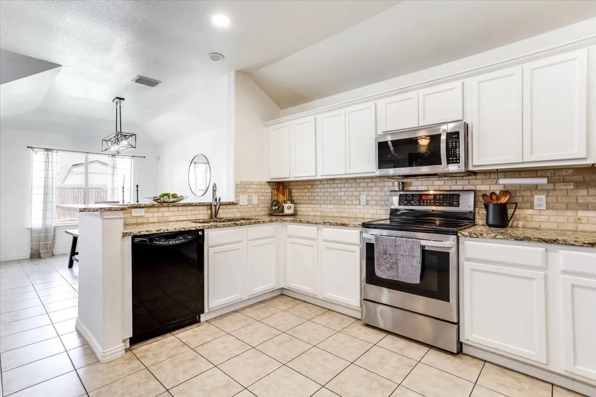 Kitchen featuring white cabinetry, light-toned tile flooring, granite countertops, a tile backsplash, and stainless steel appliances