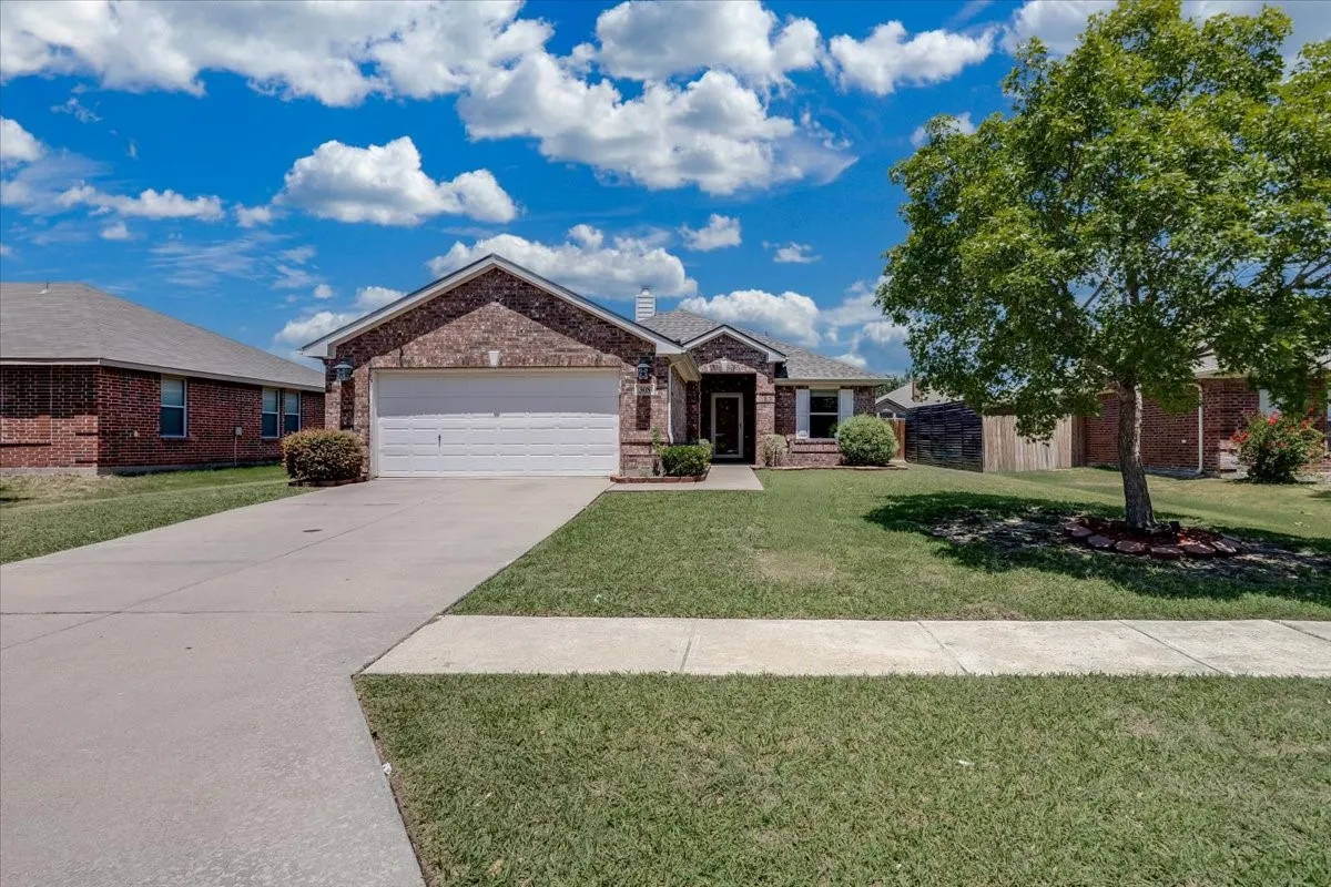 Brick exterior with a gabled roofline, attached two-car garage, mature landscaping, and an expansive concrete driveway
