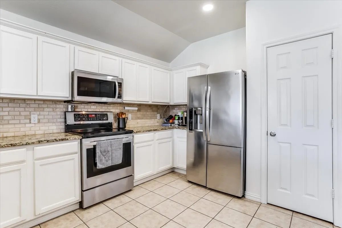 White cabinetry, light-toned tile flooring, stainless steel appliances, granite countertops, and a subway tile backsplash